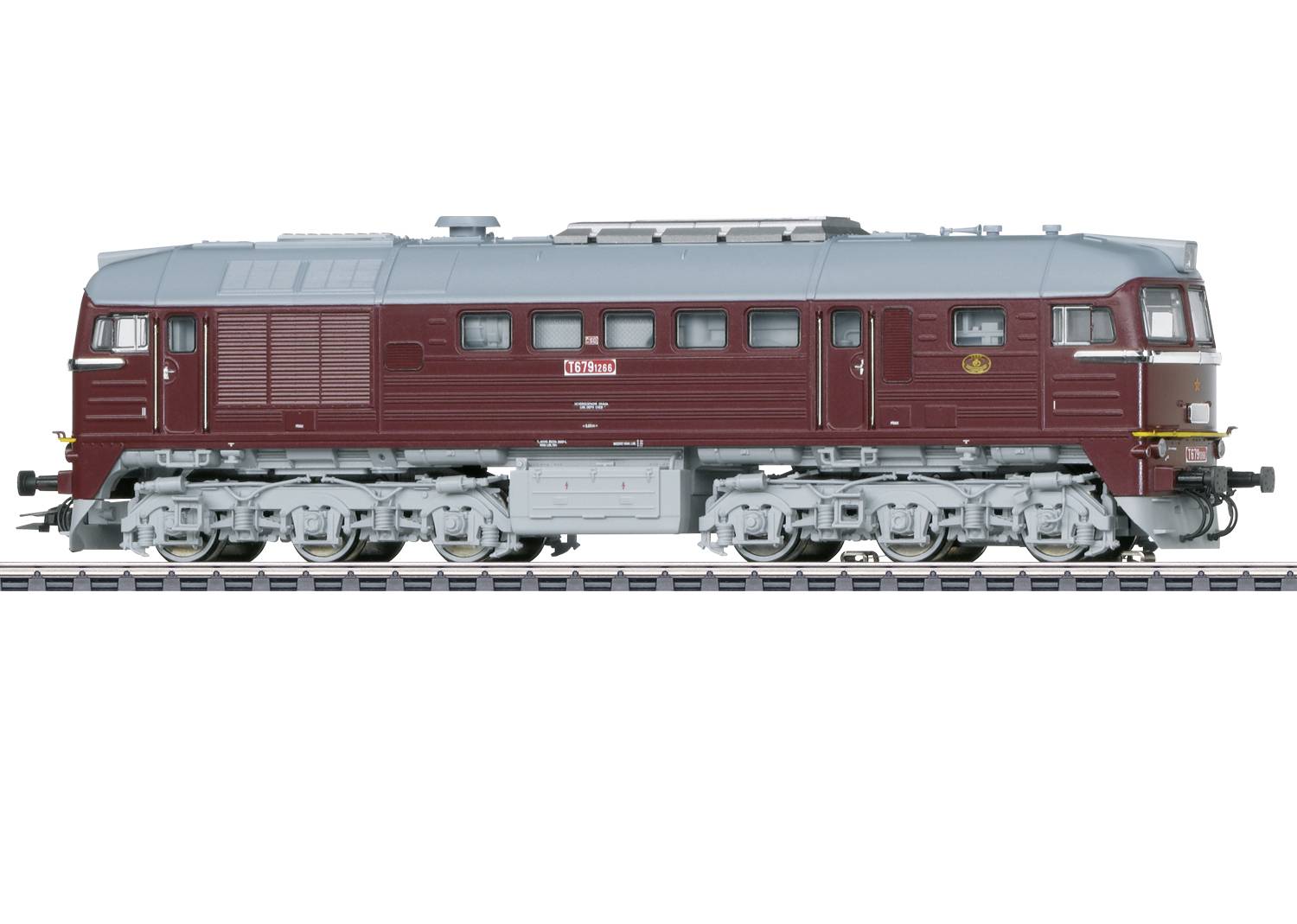 A locomotive in red and grey stands on the track. It has six axles and is robustly designed. The locomotive has a rectangular window design.
