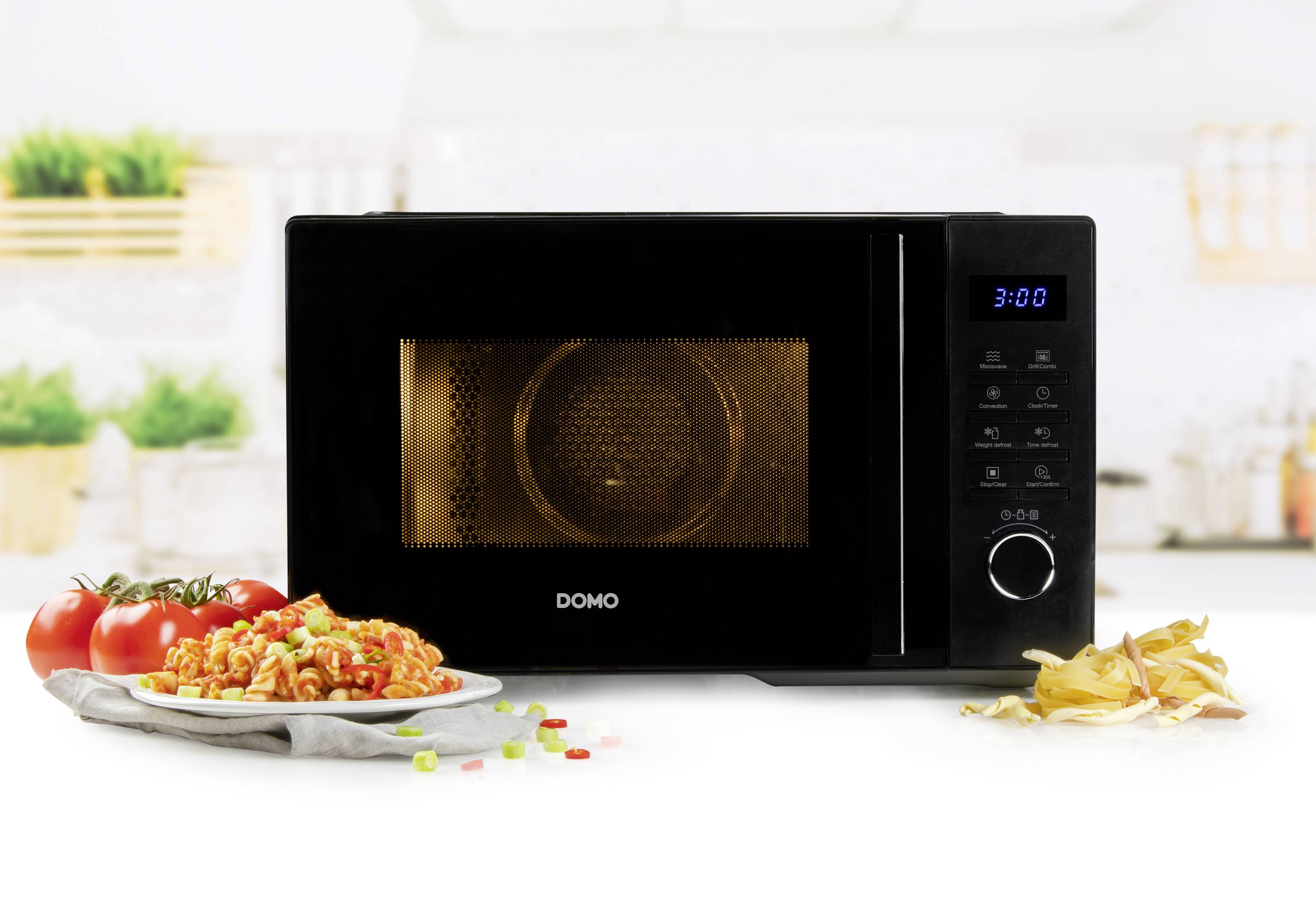 Black microwave on kitchen worktop, next to a plate of pasta and tomatoes. A blurred kitchen scene is in the background.