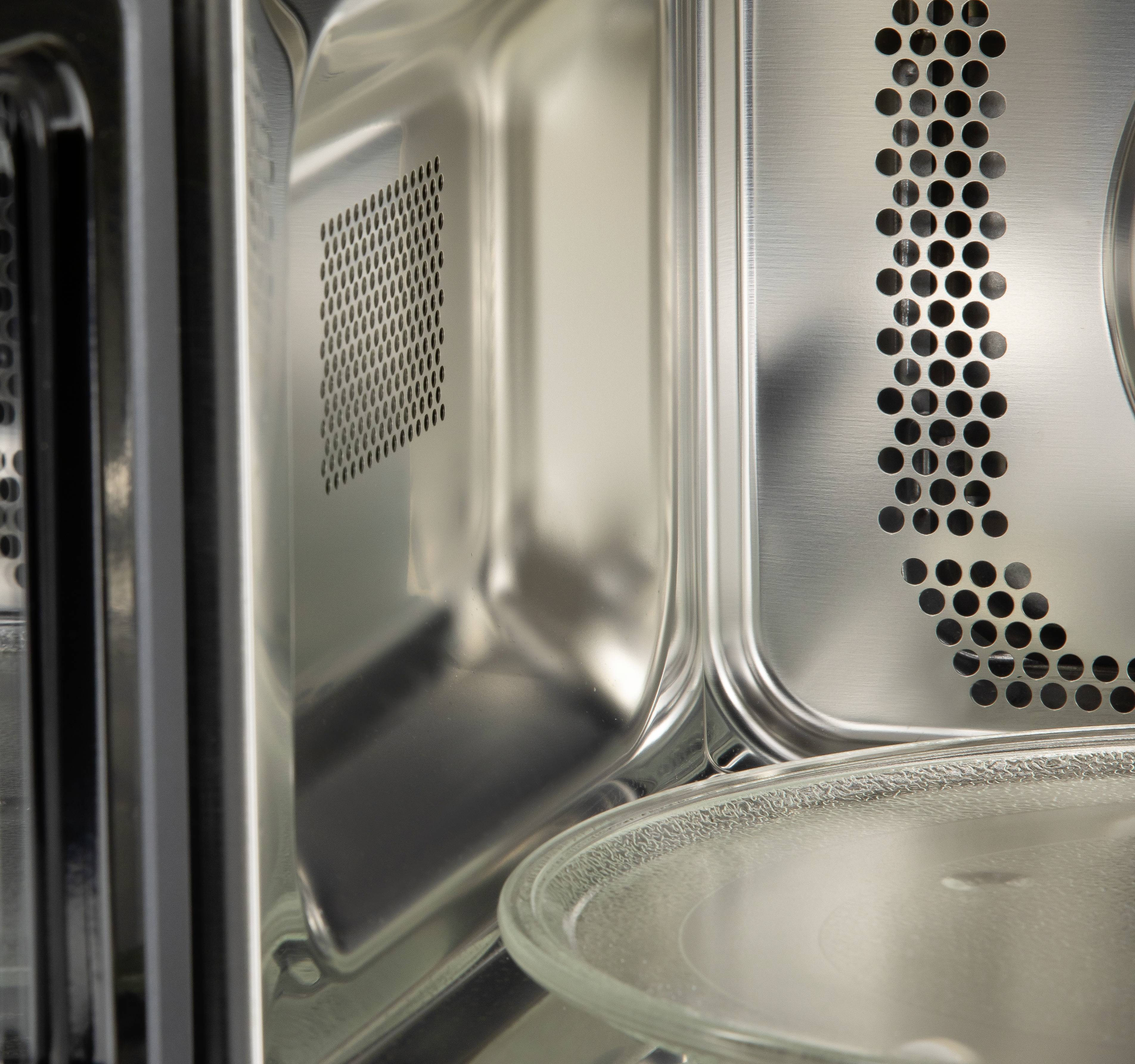 Interior of a stainless steel microwave with a turntable. Wide ventilation holes visible on the right-hand side wall.
