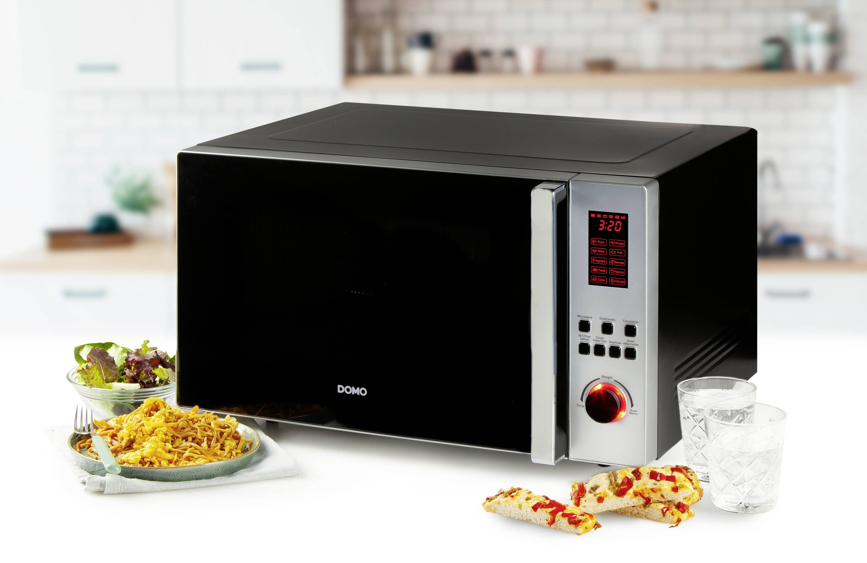Black microwave on a kitchen worktop, next to a plate with a pasta dish, pizza slices and two glasses of water.