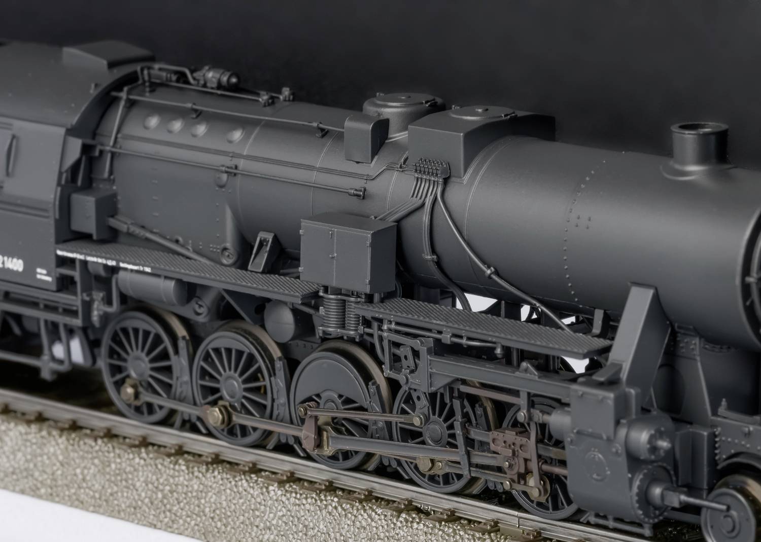 Black and grey steam locomotive on a track, showing detailed mechanical parts and structure, neutral dark background.