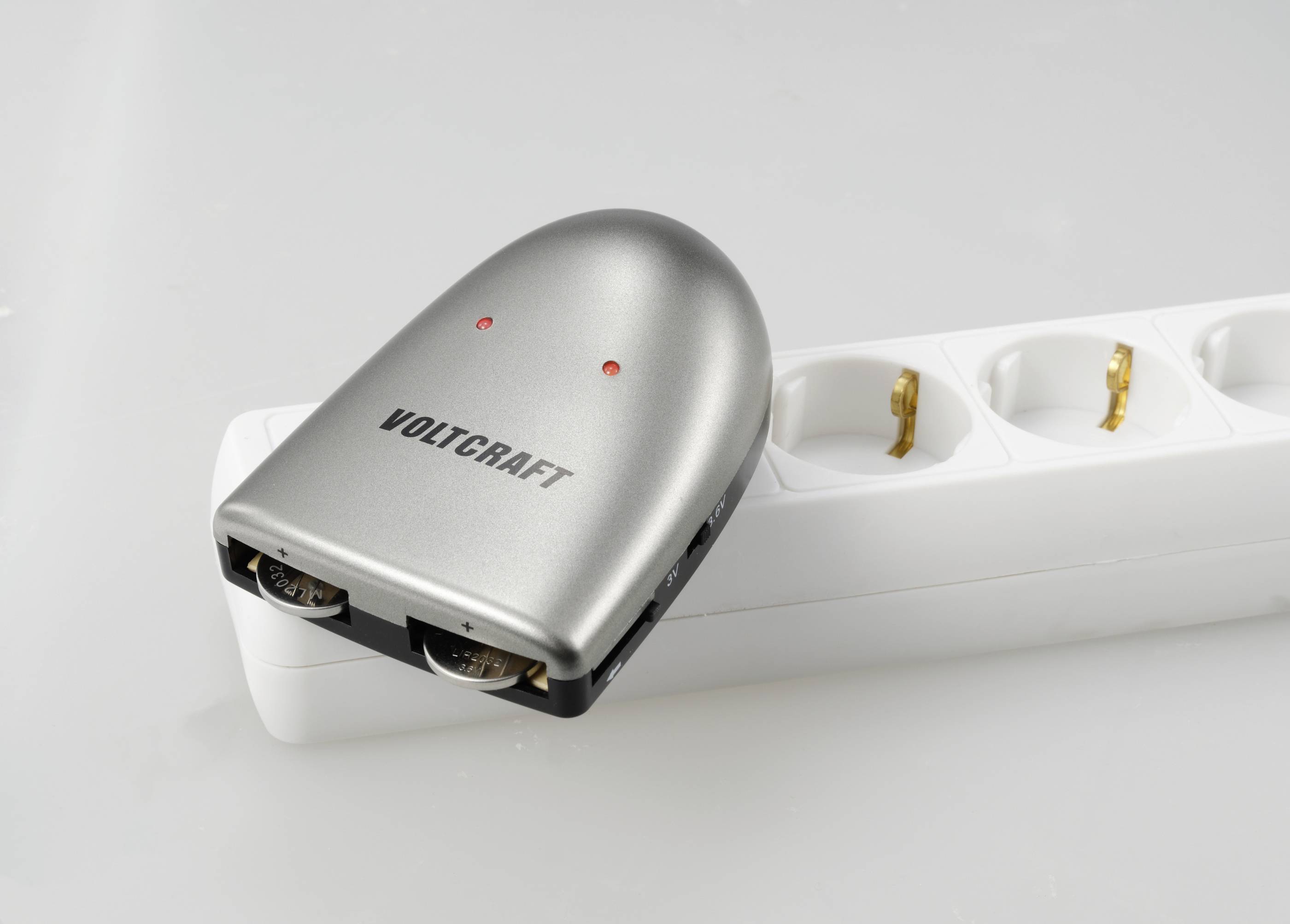 A silver Voltcraft ammeter is lying on a white multi-socket power strip.