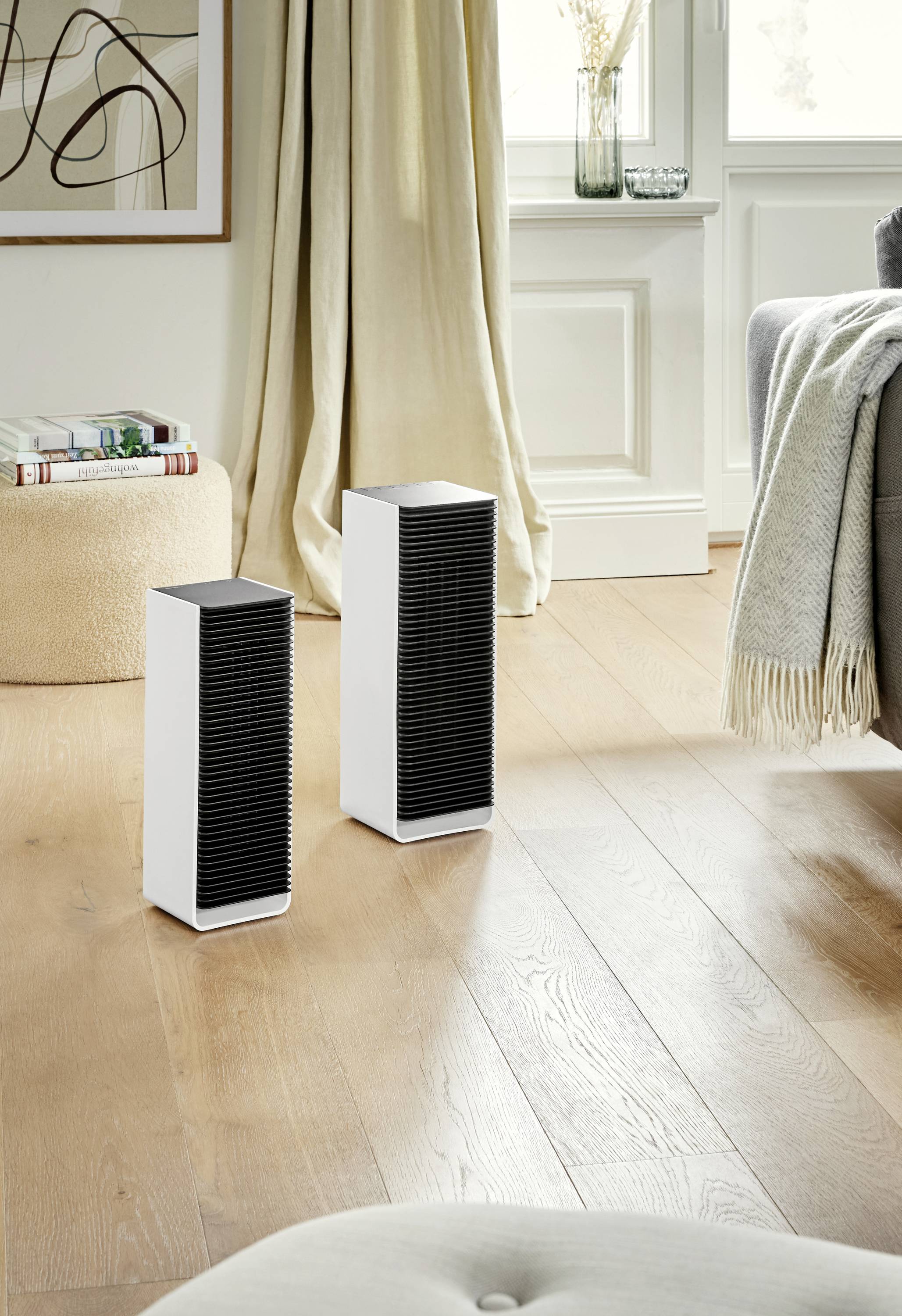 Two white speakers with black grille covers are standing on a wooden floor in a modern living room.