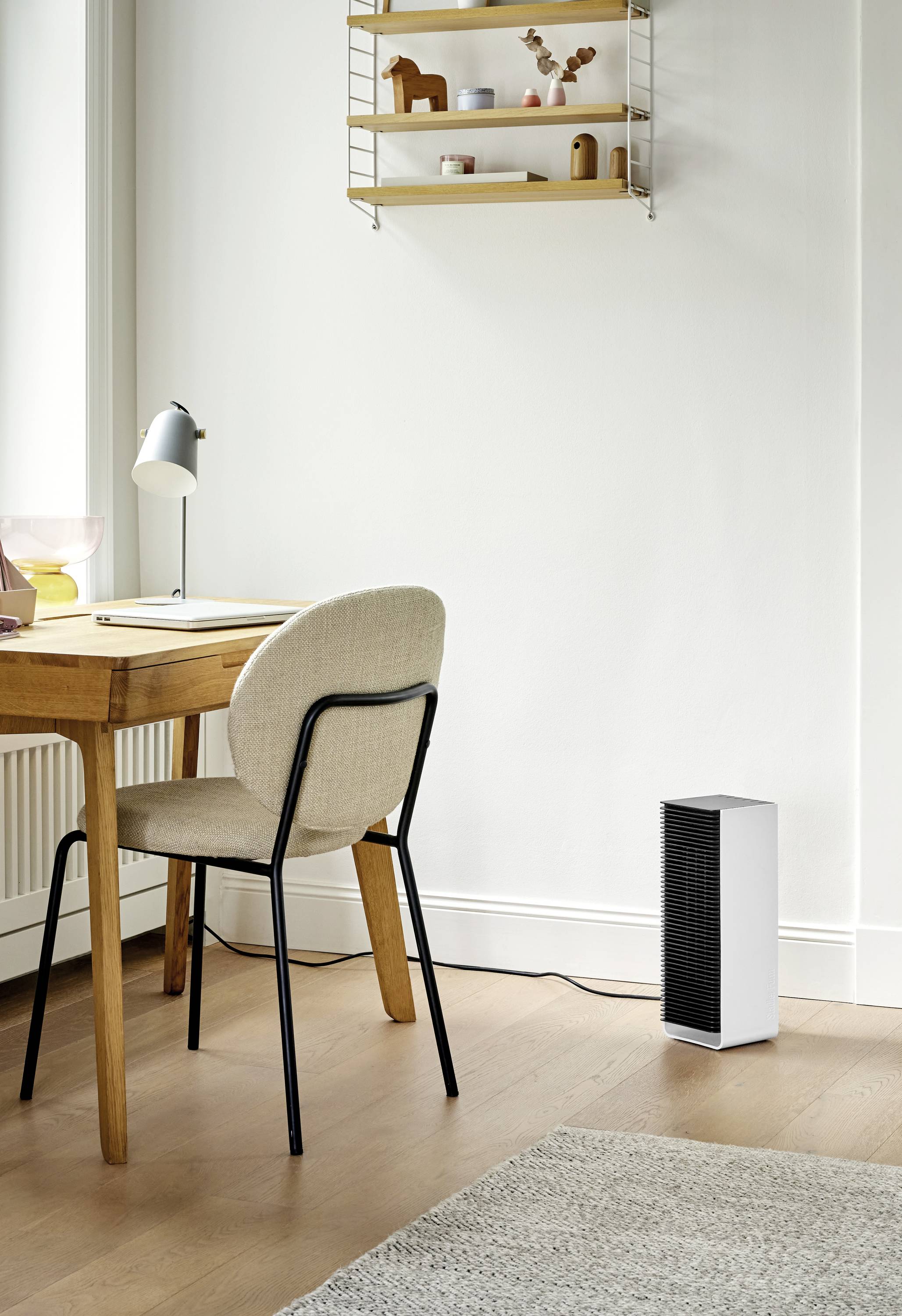 A simple office with a wooden table and chair, a shelf on the wall and an air purifier on the floor.