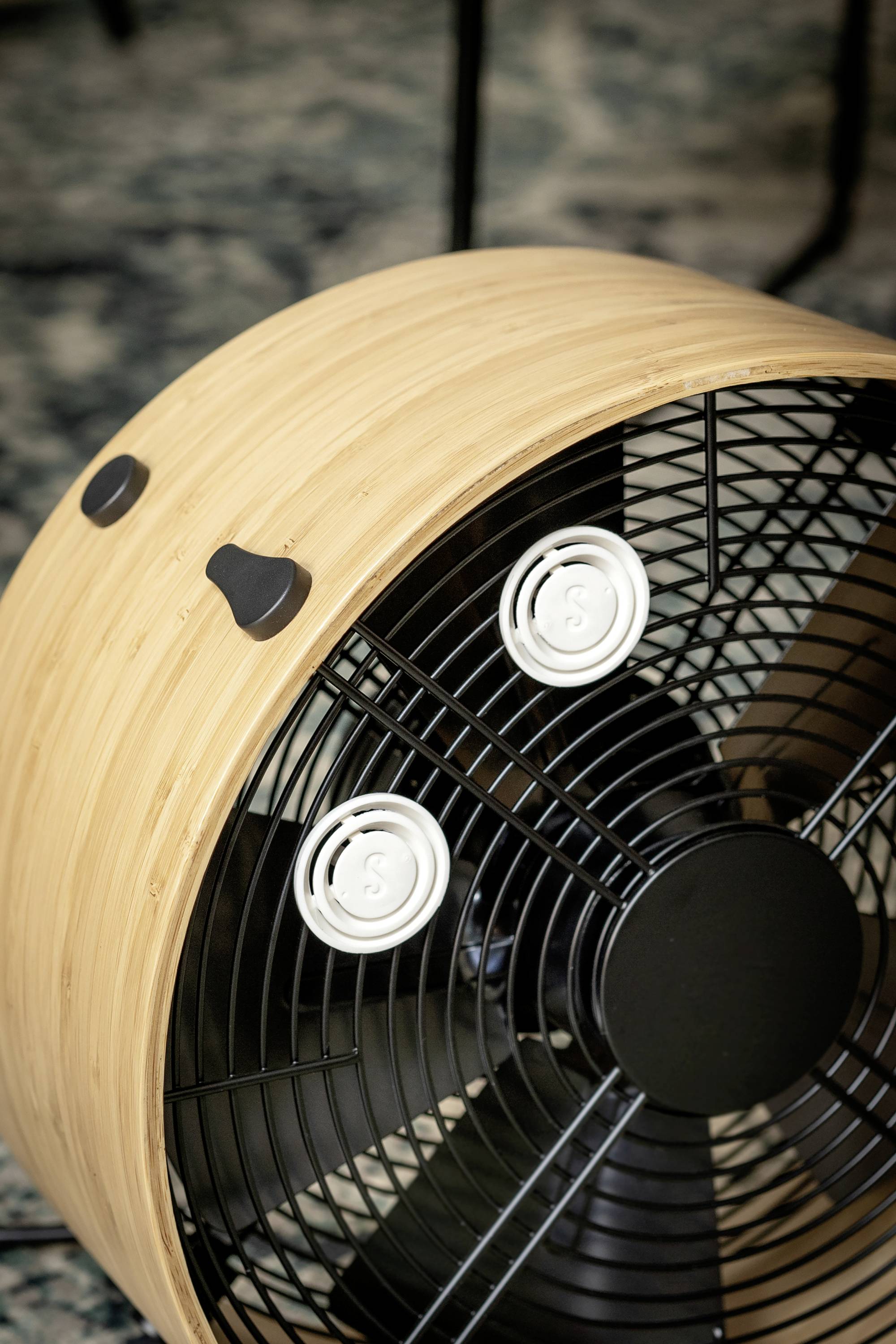 A fan with a wood-effect casing, three black rotor blades and two adjustable control knobs for speed and tilt.