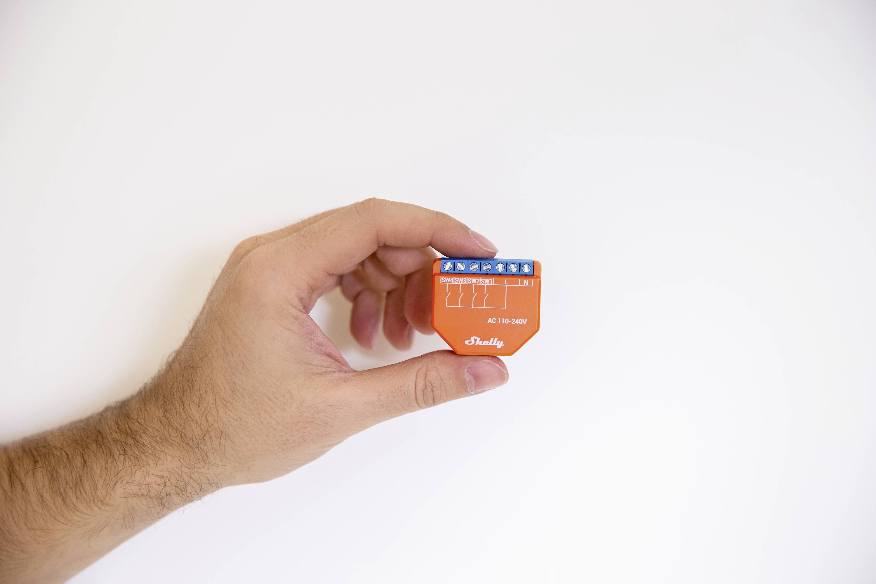 A hand is holding an orange electronic device with a blue connection strip.