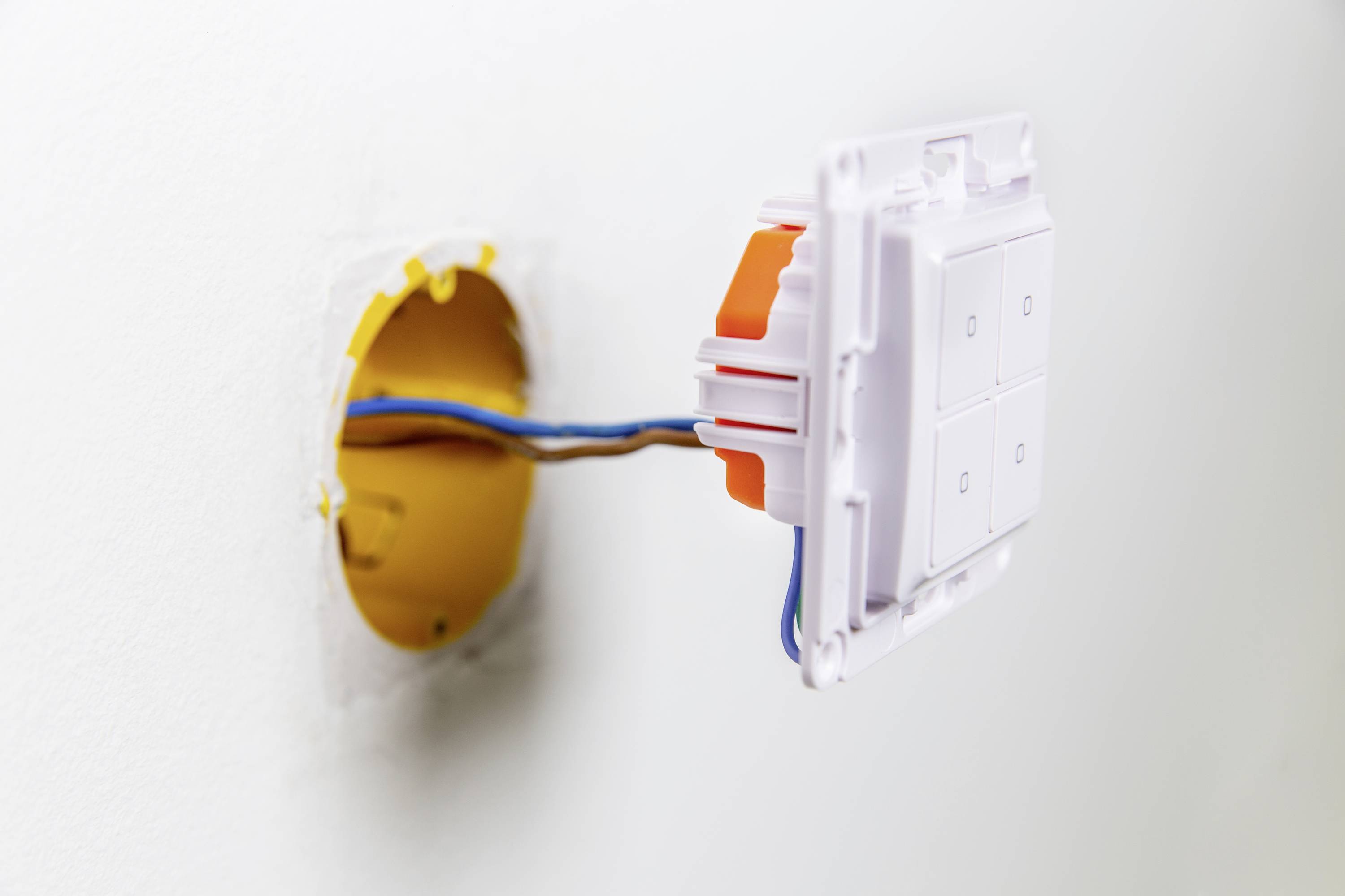 An open socket on the wall with exposed cables leading into a yellow cavity electronic housing.