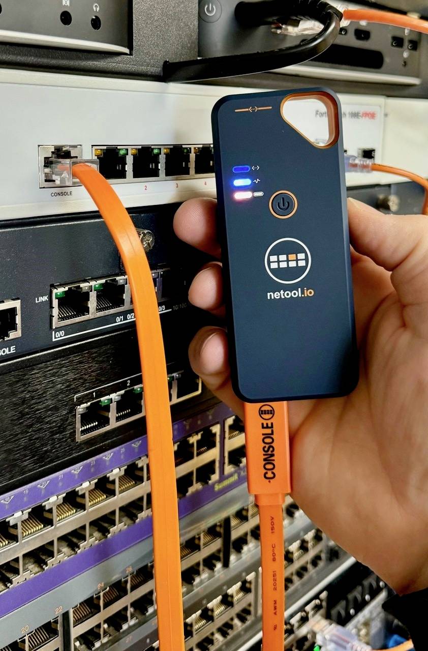 A hand holds a network analysis tool, connected with an orange cable to a rack server. LEDs on the device indicate status.