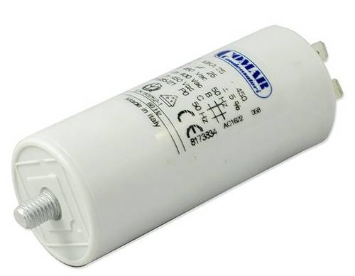 A cylindrical capacitor with a white casing and printed markings, including technical symbols and values, is resting on a surface.