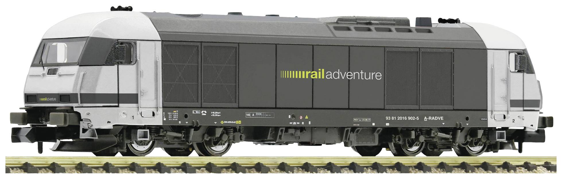 A modern locomotive with the inscription 'rail adventure' on its side stands on railway tracks. The design is black and white.