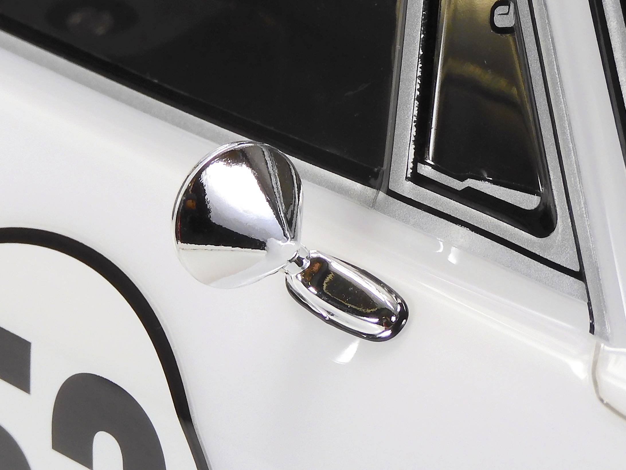 Close-up of a gleaming car wing mirror on a white vehicle, with a black number '56' on its door.