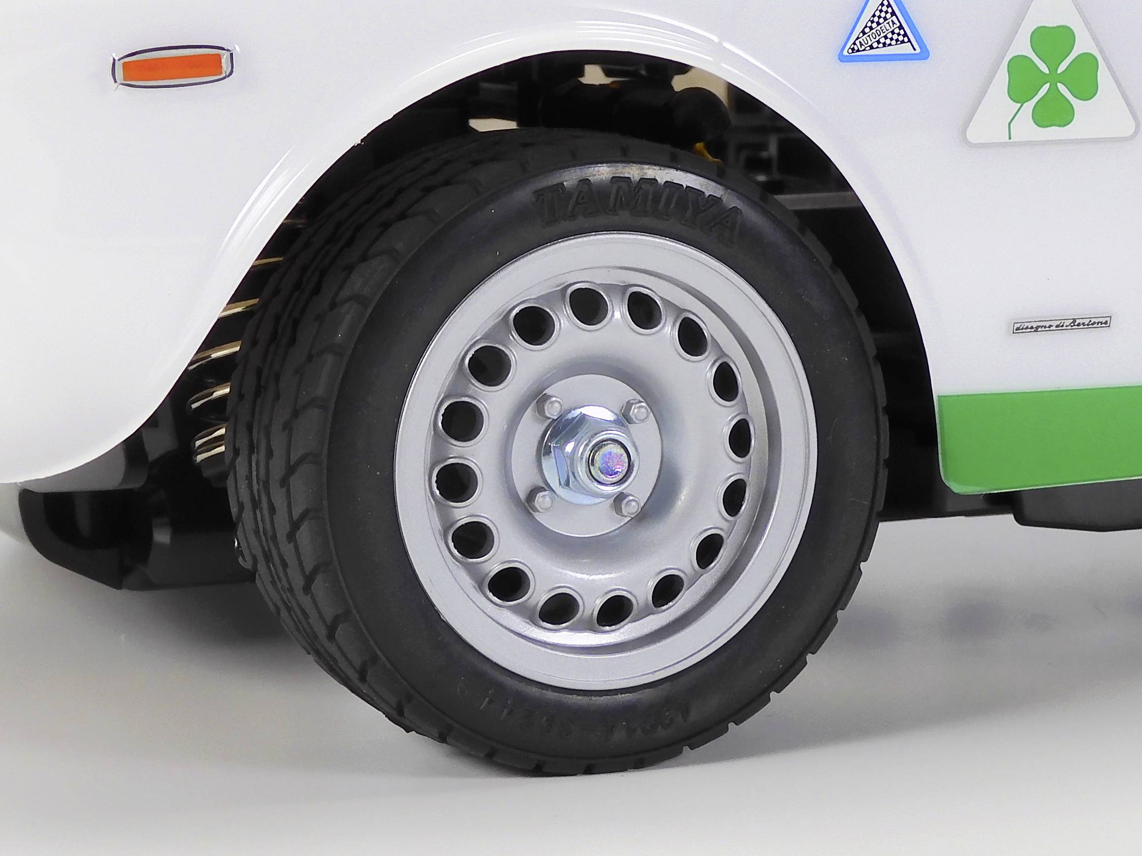 Close-up of a white car with an aluminium wheel and black tyre. A green four-leaf clover logo is displayed on the wing.
