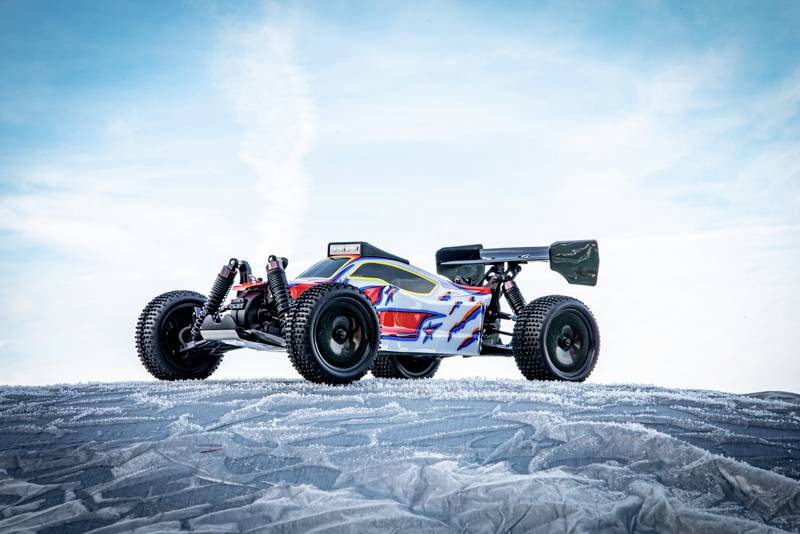A remote-controlled car with a colourful design sits on an icy surface against a blue sky.
