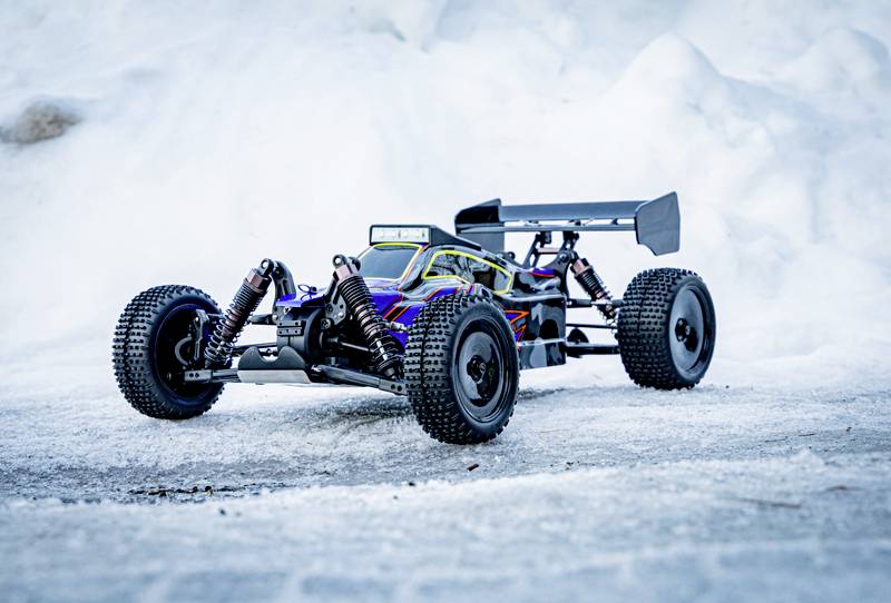 A remote-controlled car drives across snow-covered terrain. It has wide tyres and a sporty design. Background of snow.