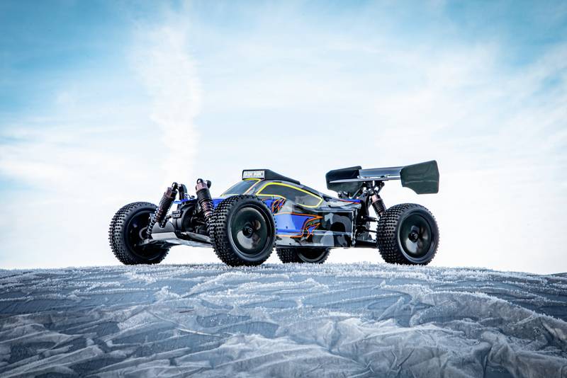 A remote-controlled car with a colourful design sits on a snow-covered surface against a blue sky.