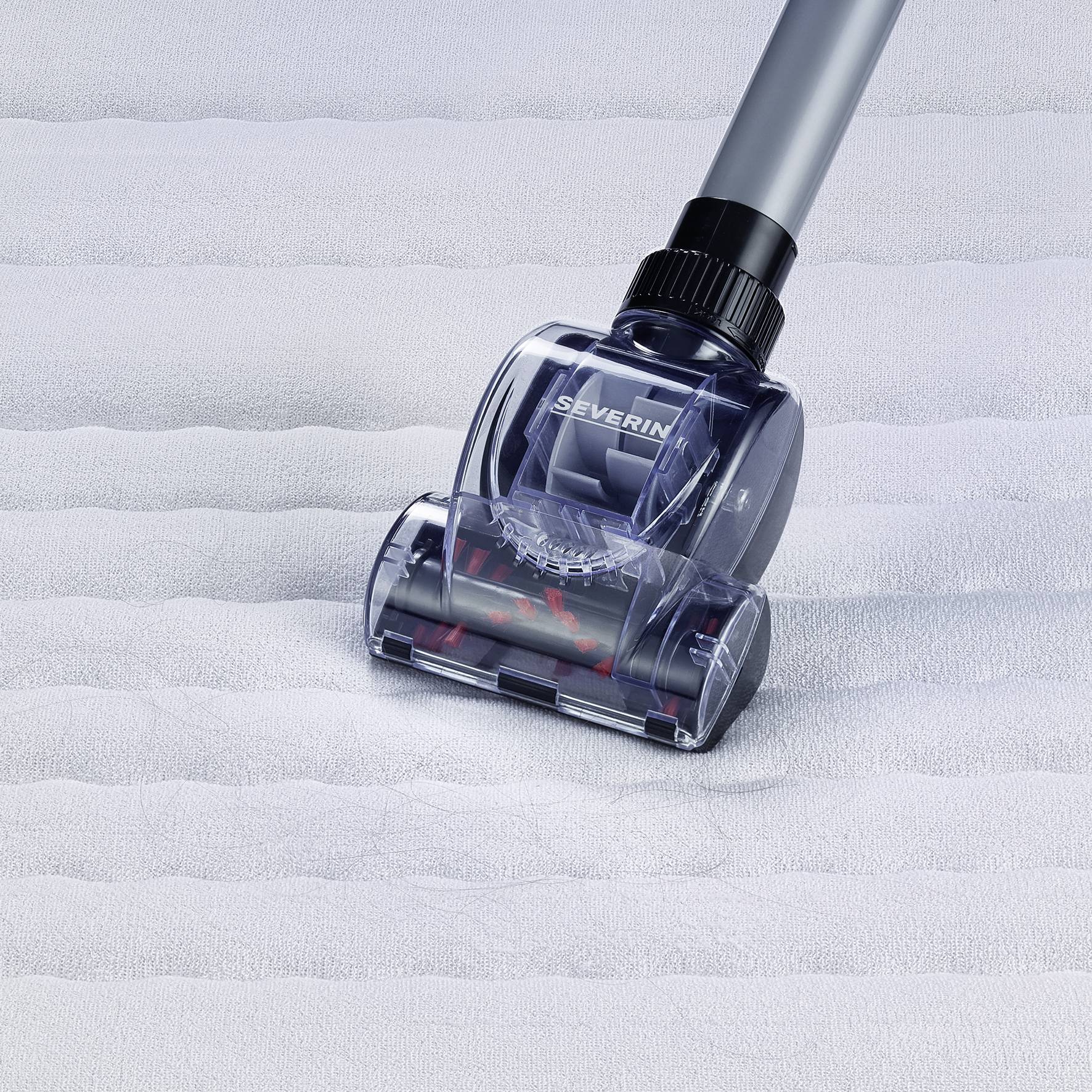 A vacuum cleaner head is hovering over a white, textured surface. It is transparent and reveals a rotating brush.