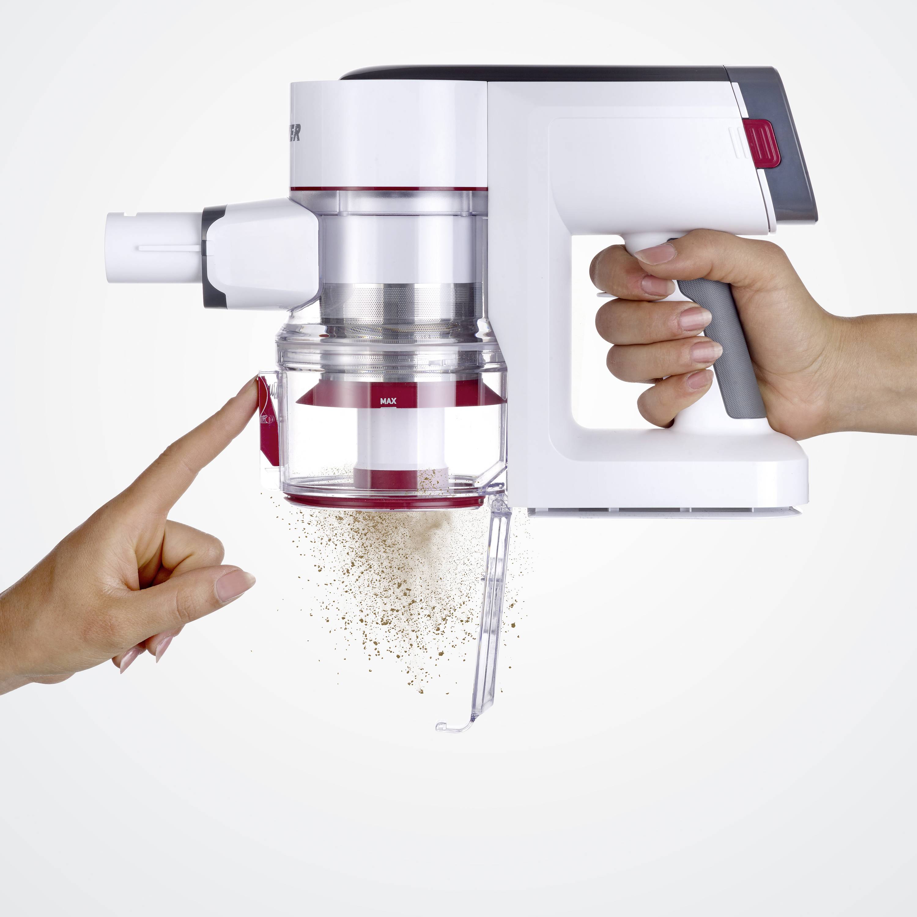 A hand is holding a vacuum cleaner while another hand points to a partially emptied dust container. Dust is falling out.