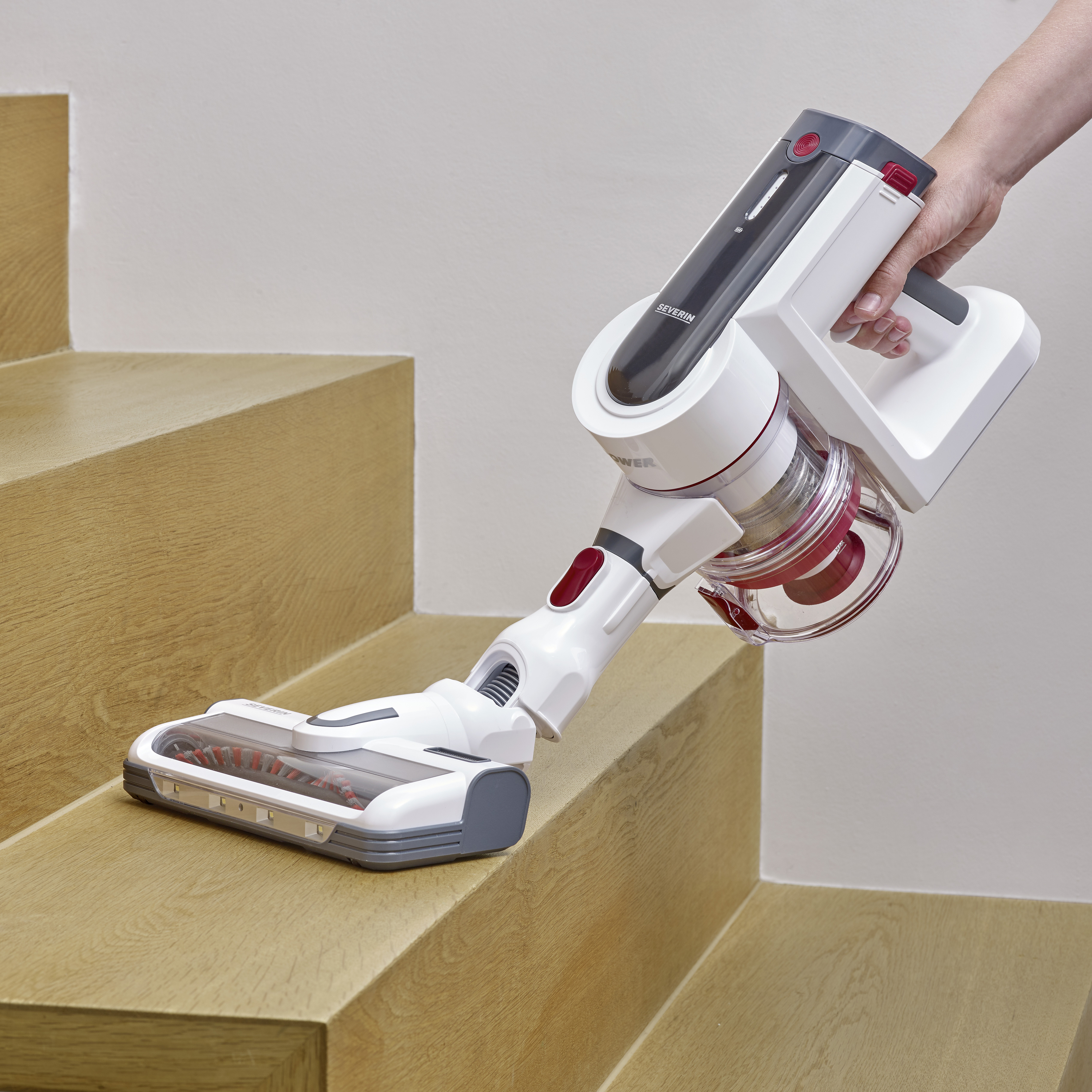 A person is cleaning stair steps with a cordless, handheld vacuum cleaner on a wooden staircase. Focus on efficiency and ergonomics.