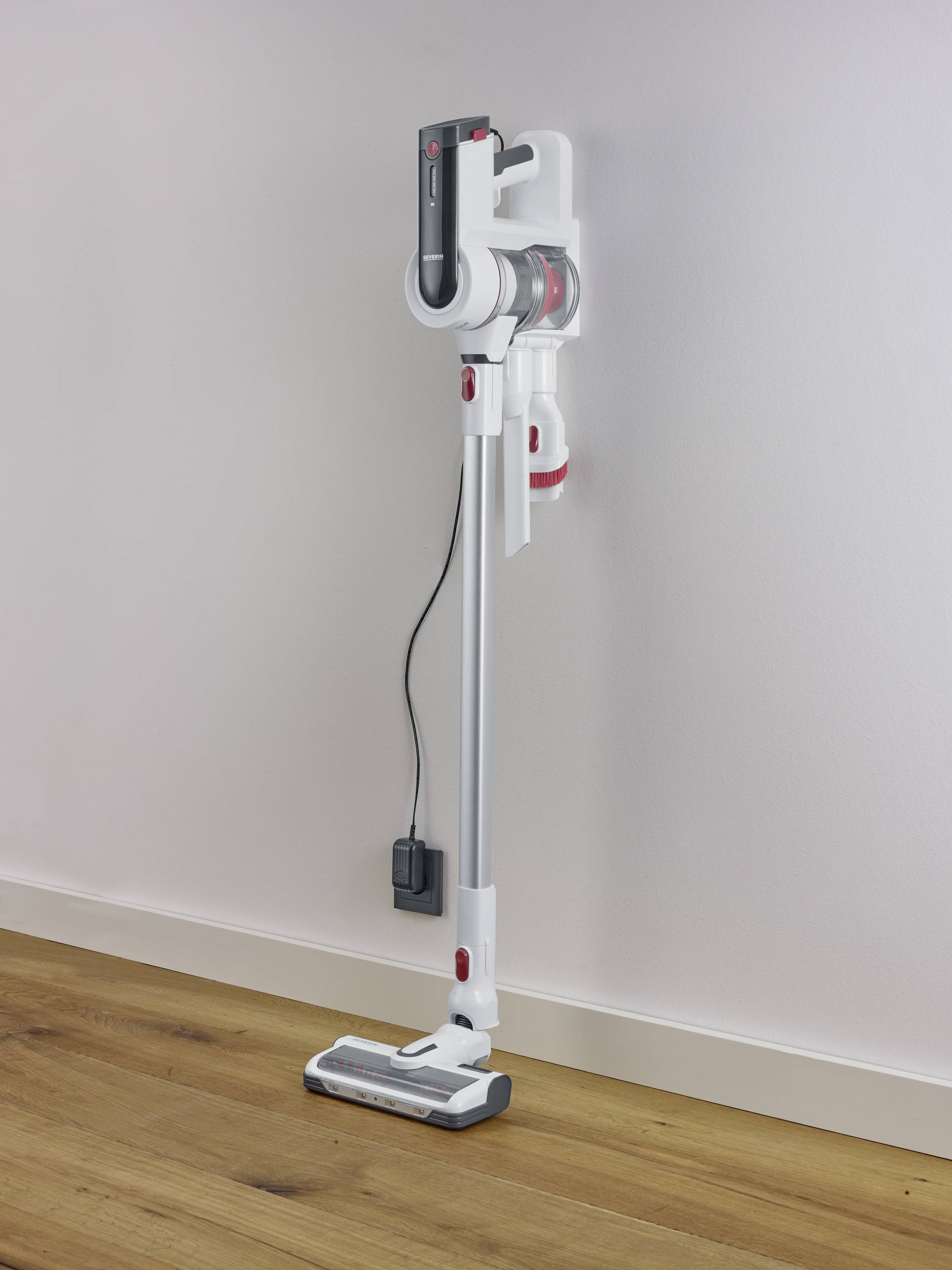 Cordless, white vacuum cleaner stands upright against a wall, with charging station attached to the side. Suitable for modern households.