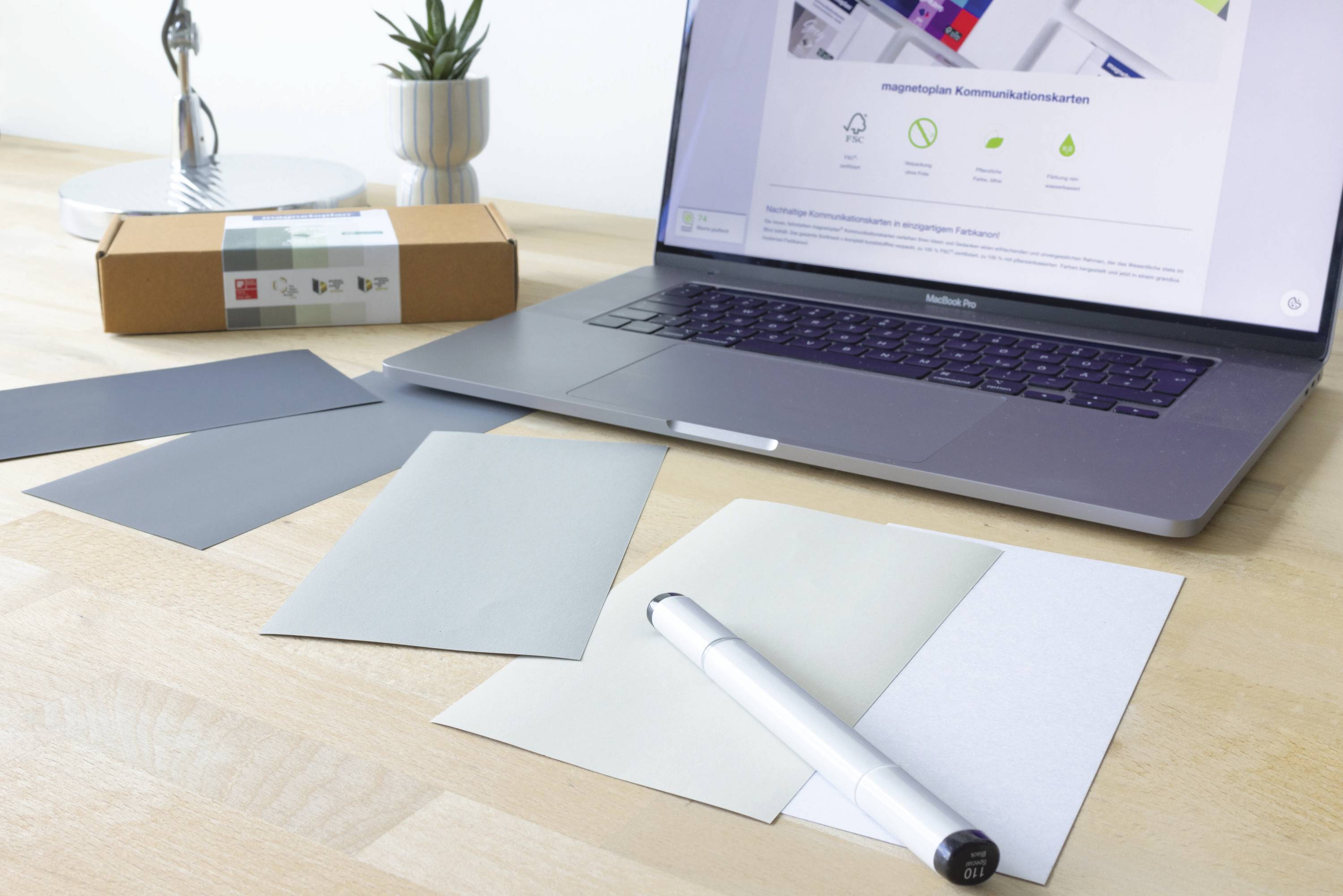 A laptop is displaying a webpage about modern communication; colour swatches and a pen are lying beside it on a desk.