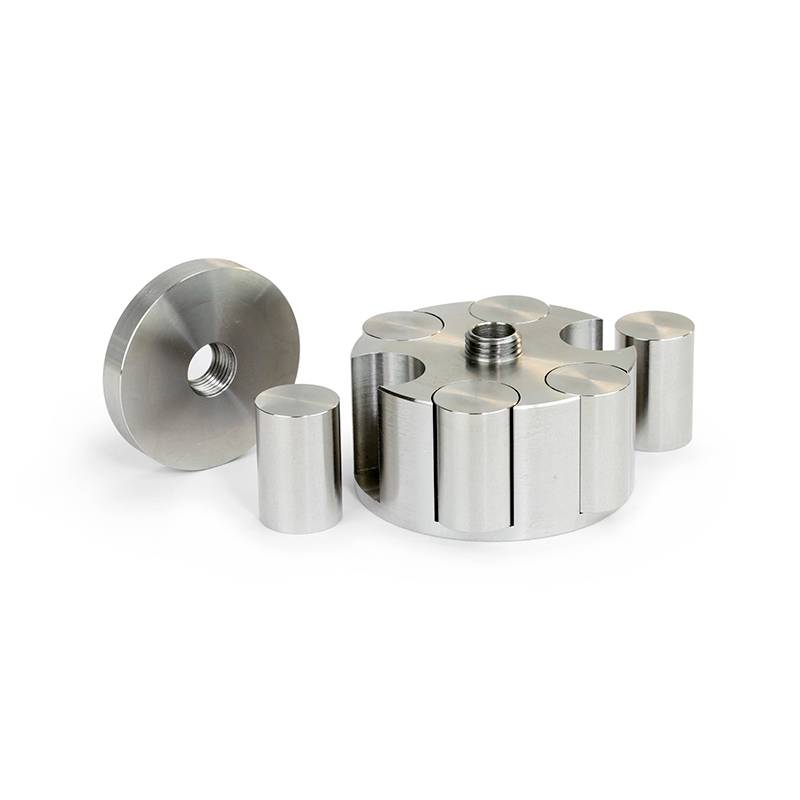 A cylindrical metal adapter with a thread, surrounded by six equally sized cylindrical metal parts on a white surface.