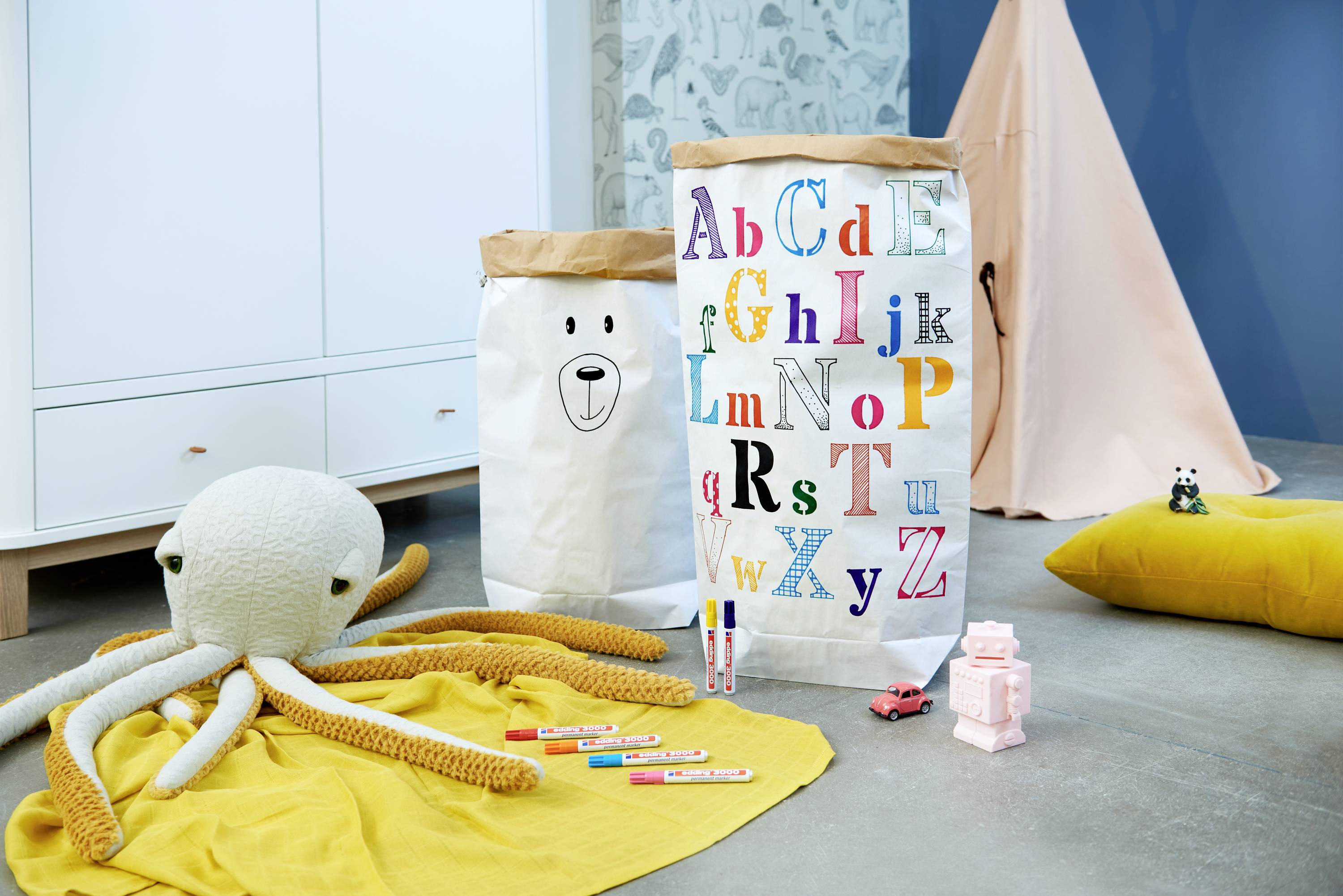 Playroom with colourful letters on cushions, a stuffed octopus on the carpet, a toy car and building blocks. A children's tent in the background.