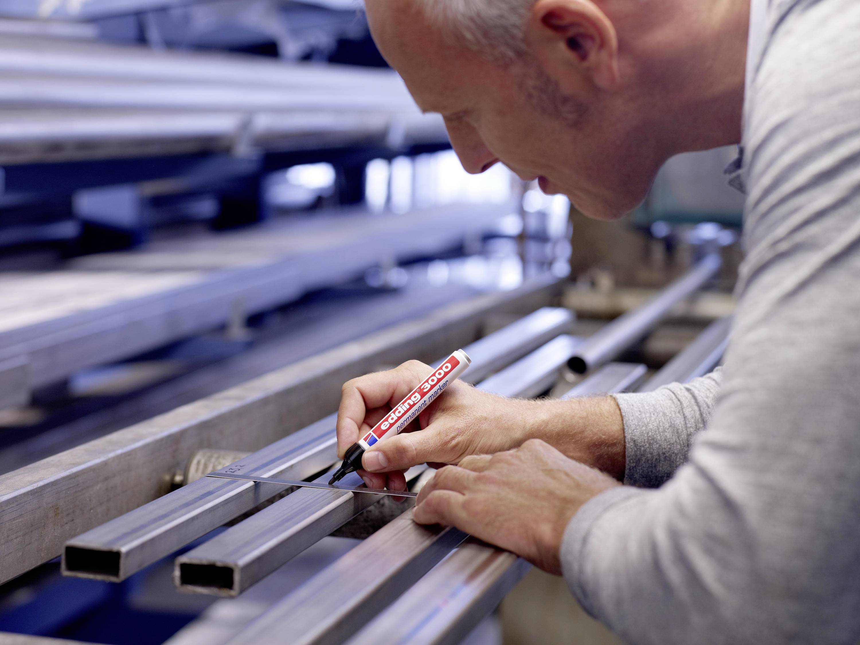 A man is marking metal pipes with a red pen in a workshop.