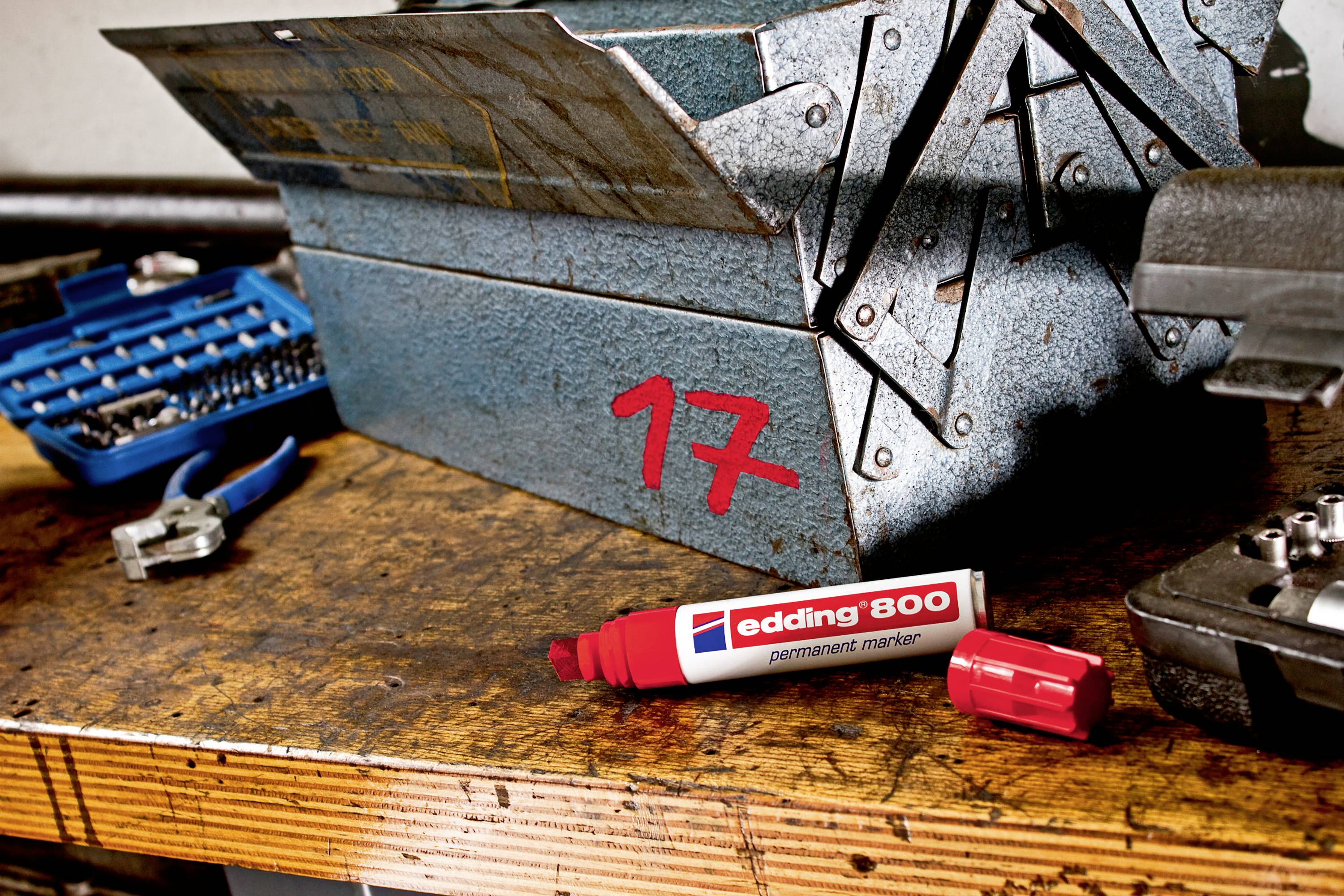 A blue toolbox is sitting on a wooden table. Next to it lies a red 'edding 800' permanent marker, with its cap removed.