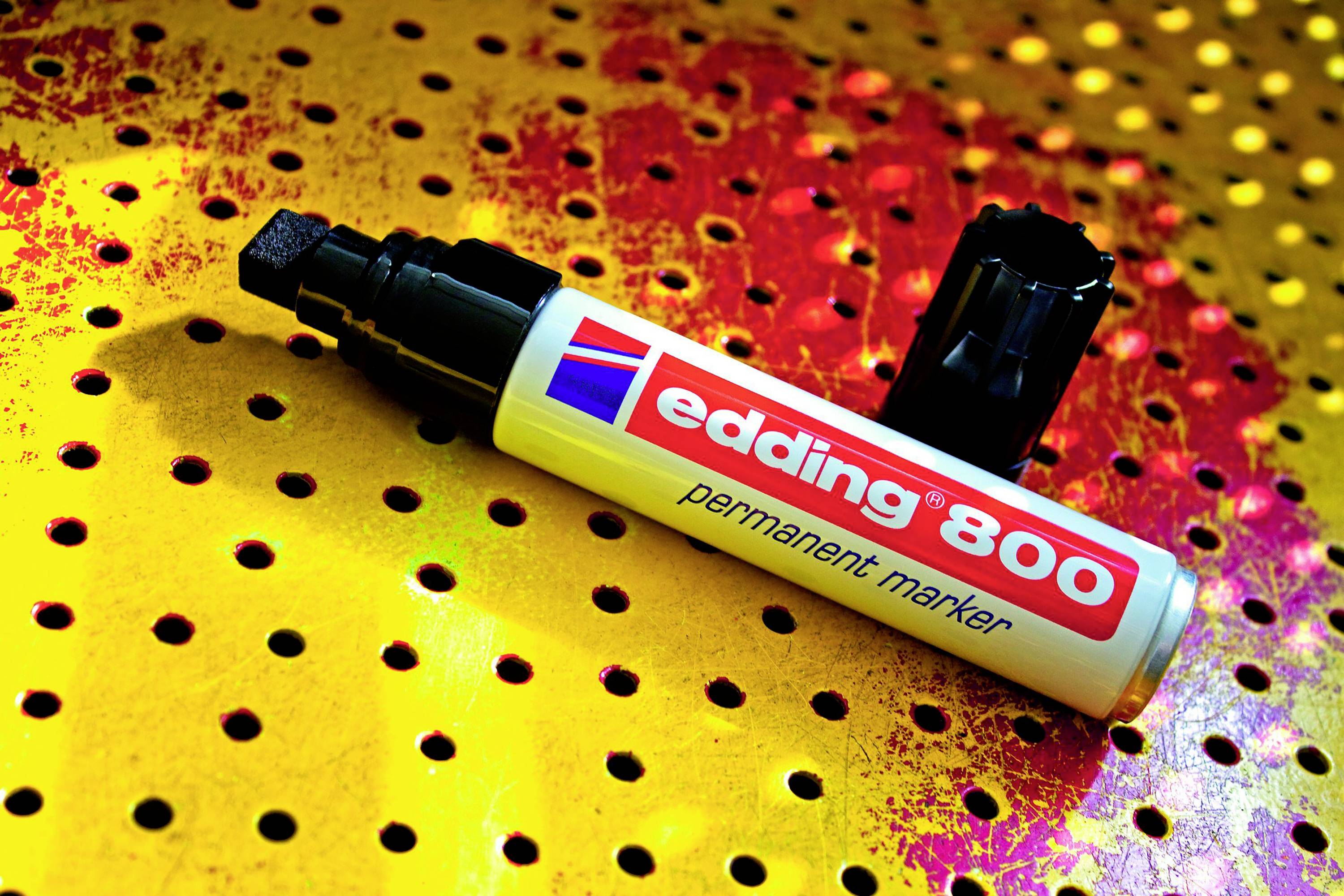 A white 'edding 800' permanent marker lies open on a colourfully speckled, perforated surface.