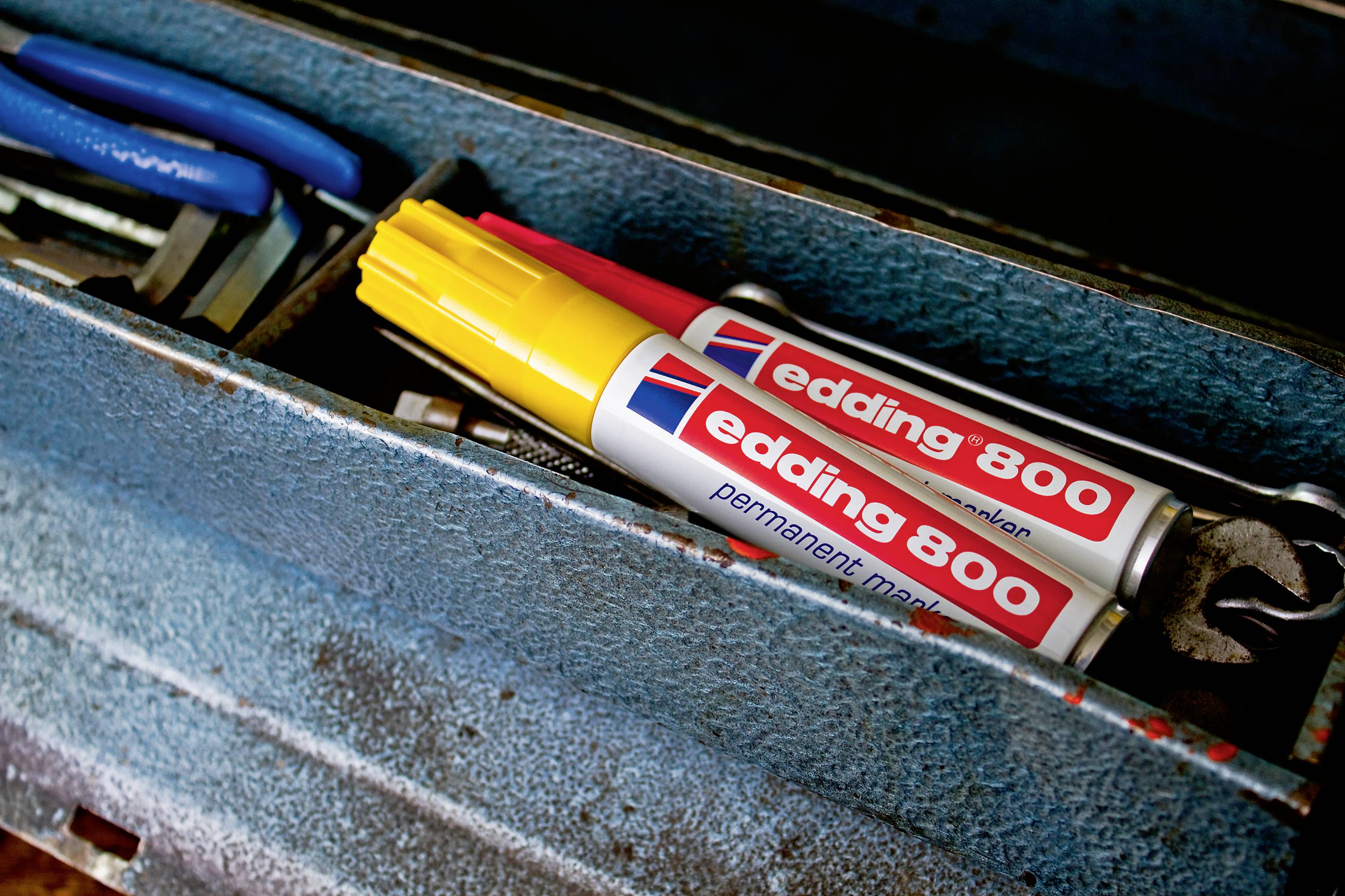 In an open blue toolbox, two yellow 'edding 800 permanent marker' pens lie next to a pair of pliers.