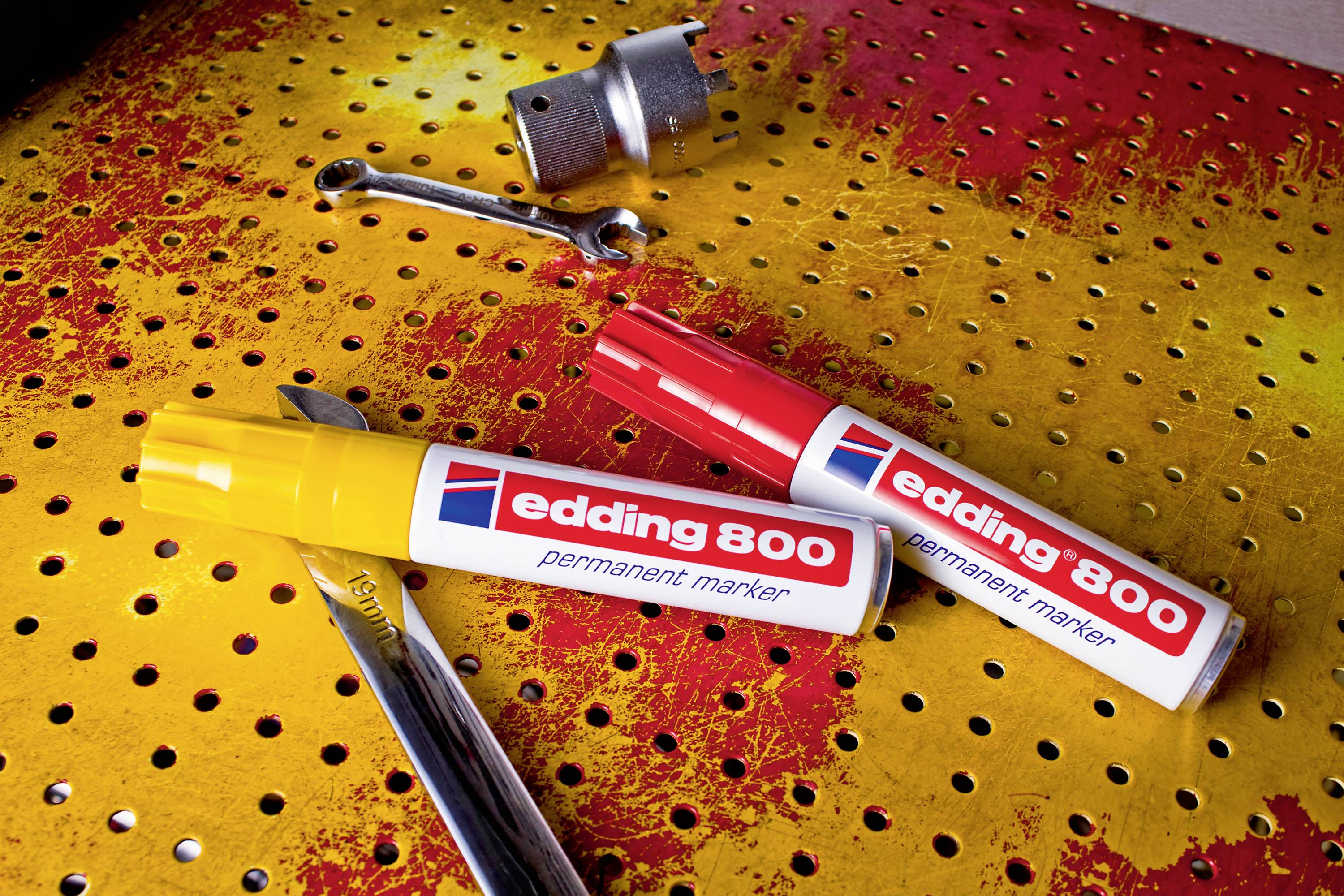 Two Edding 800 permanent markers, one yellow and one red, are lying on a yellow perforated board, surrounded by spanners and a pen.