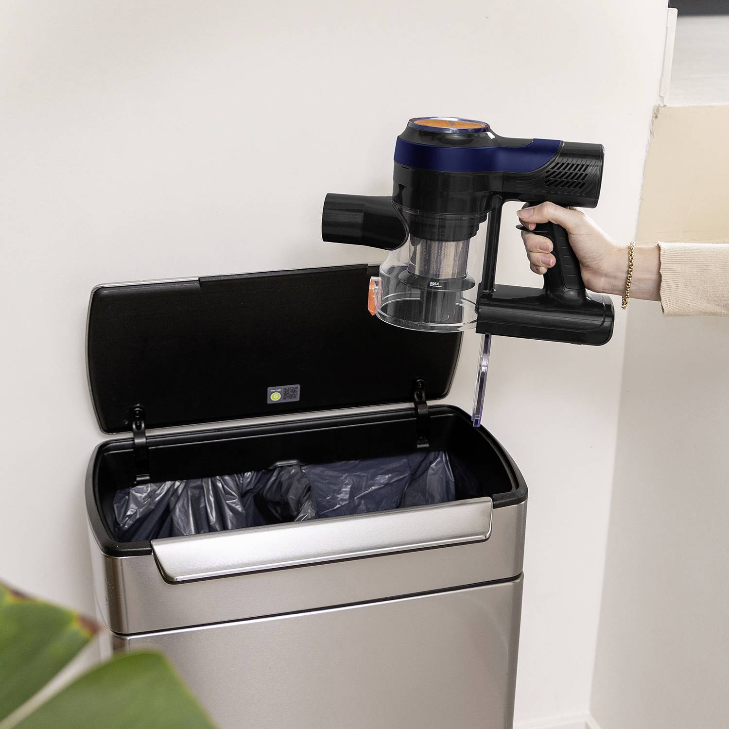 A person empties a handheld vacuum cleaner into a bin in a modern room.