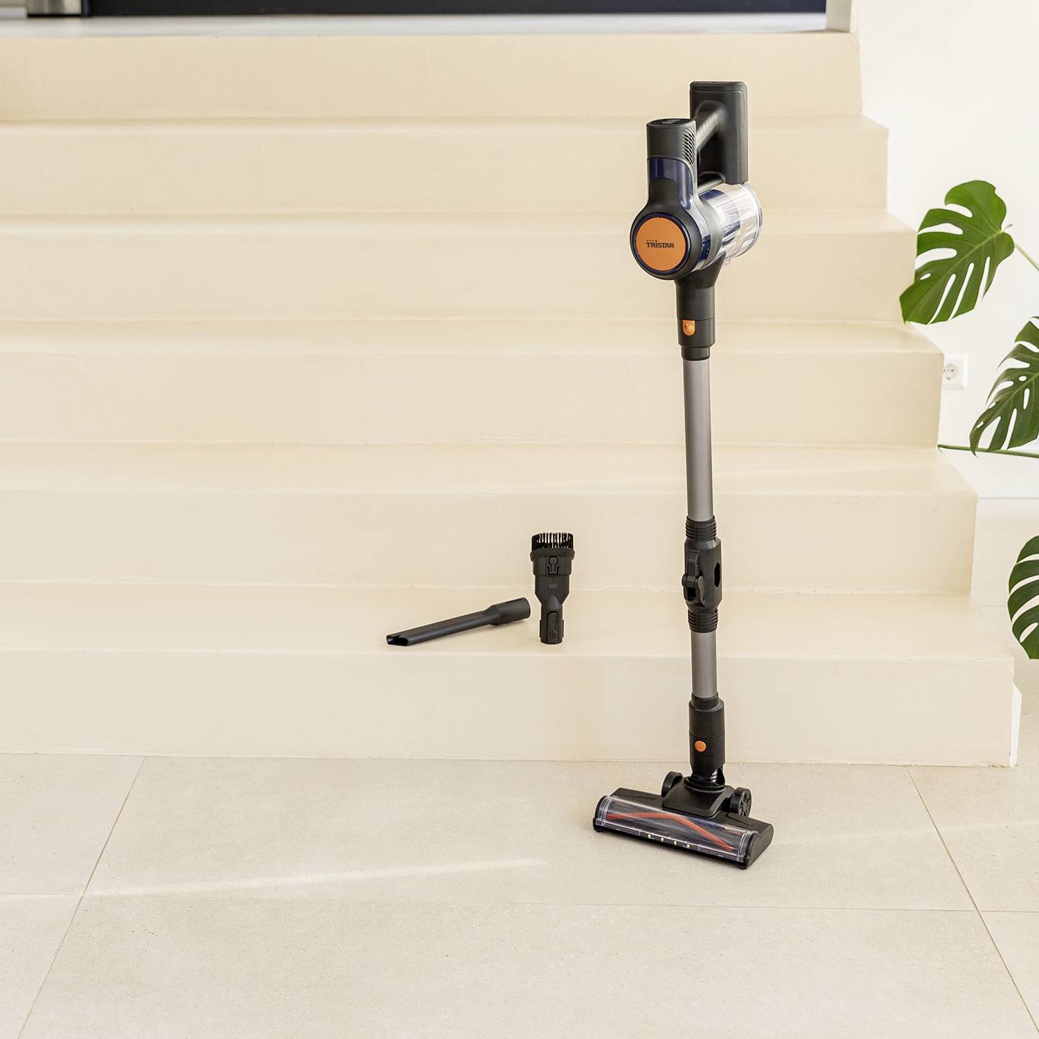 A cordless vacuum cleaner stands on white steps, next to two interchangeable nozzles.