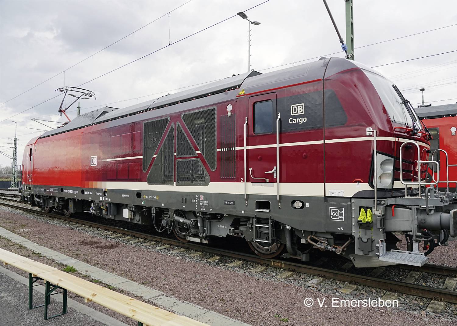 A red locomotive from DB Cargo is standing on a railway track. It is equipped with various technical components.