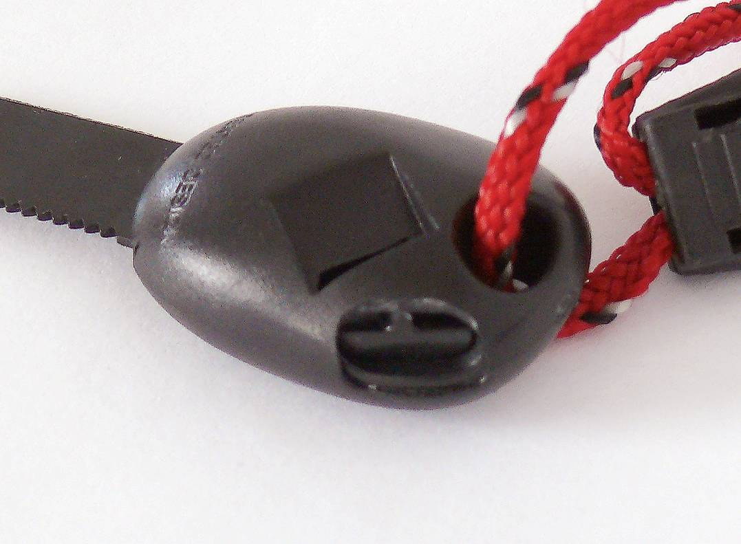 A black plastic cord stopper with a red cord running through its openings, lying on a white surface.