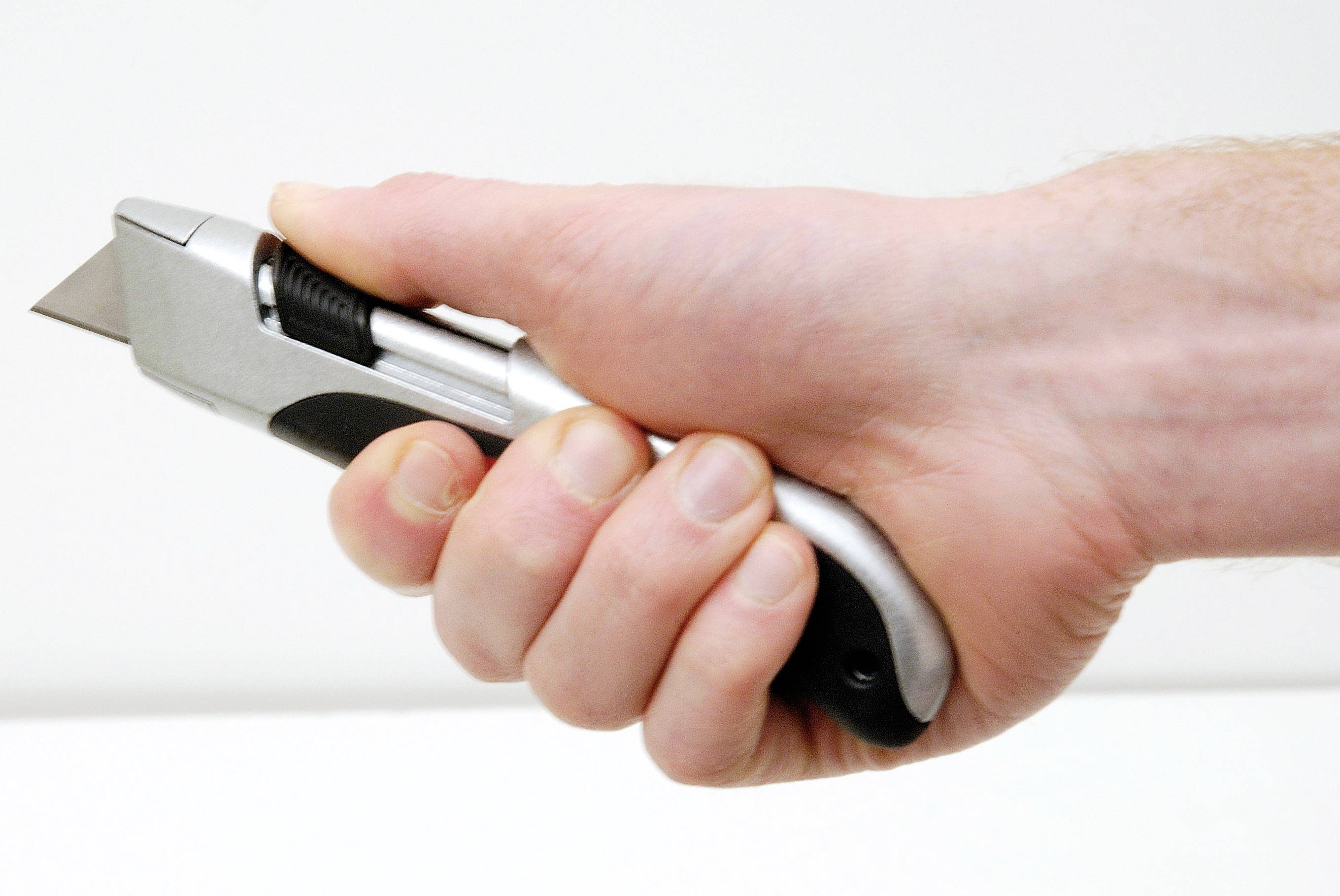 A hand is holding a silver universal can opener with a black handle. The opener is pointing forwards.