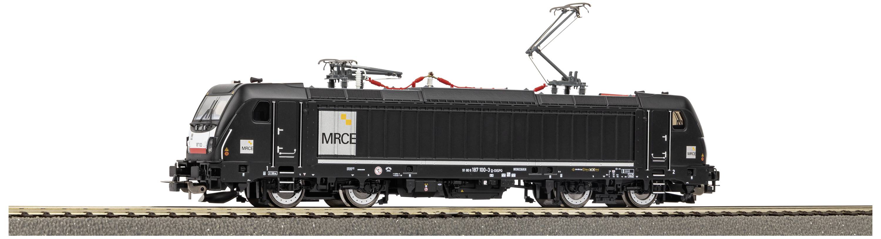 A black model railway locomotive with red details and MRC logo, standing on a track. The locomotive is equipped with overhead wires.