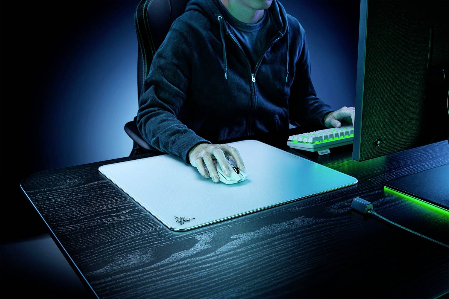 A person wearing a dark hoodie is using a computer. The scene is illuminated in blue, emphasising technology use in a modern environment.