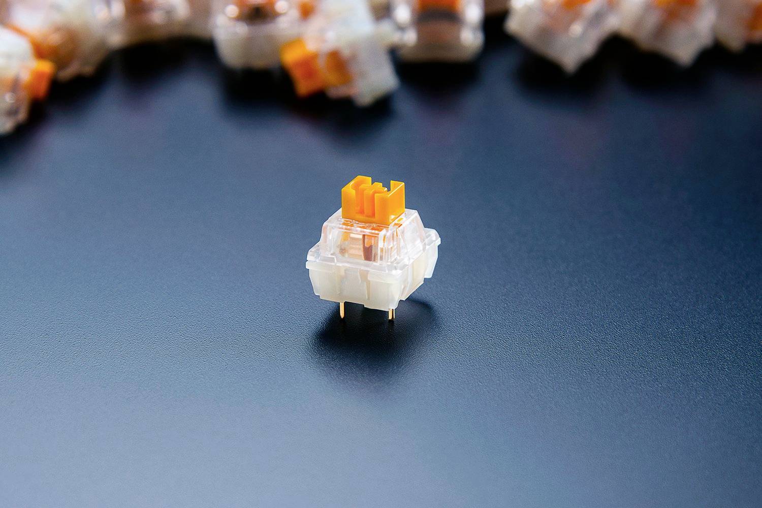 A mechanical key switch with an orange stamp is in the foreground, surrounded by additional switches in the background.