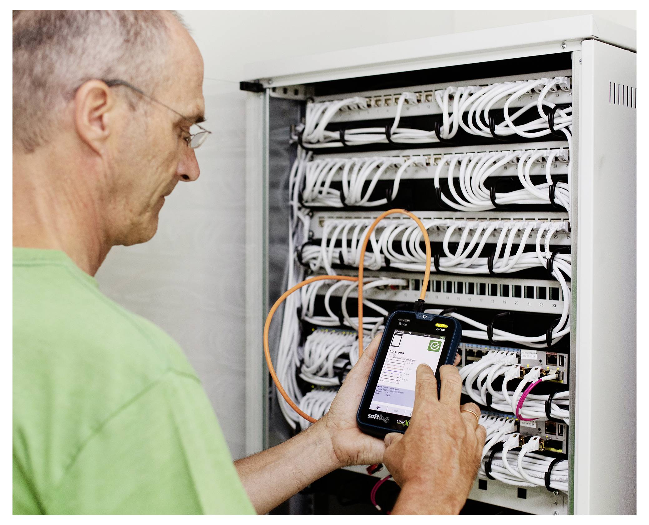 Technician using a smartphone to inspect and troubleshoot network cables in a server rack.