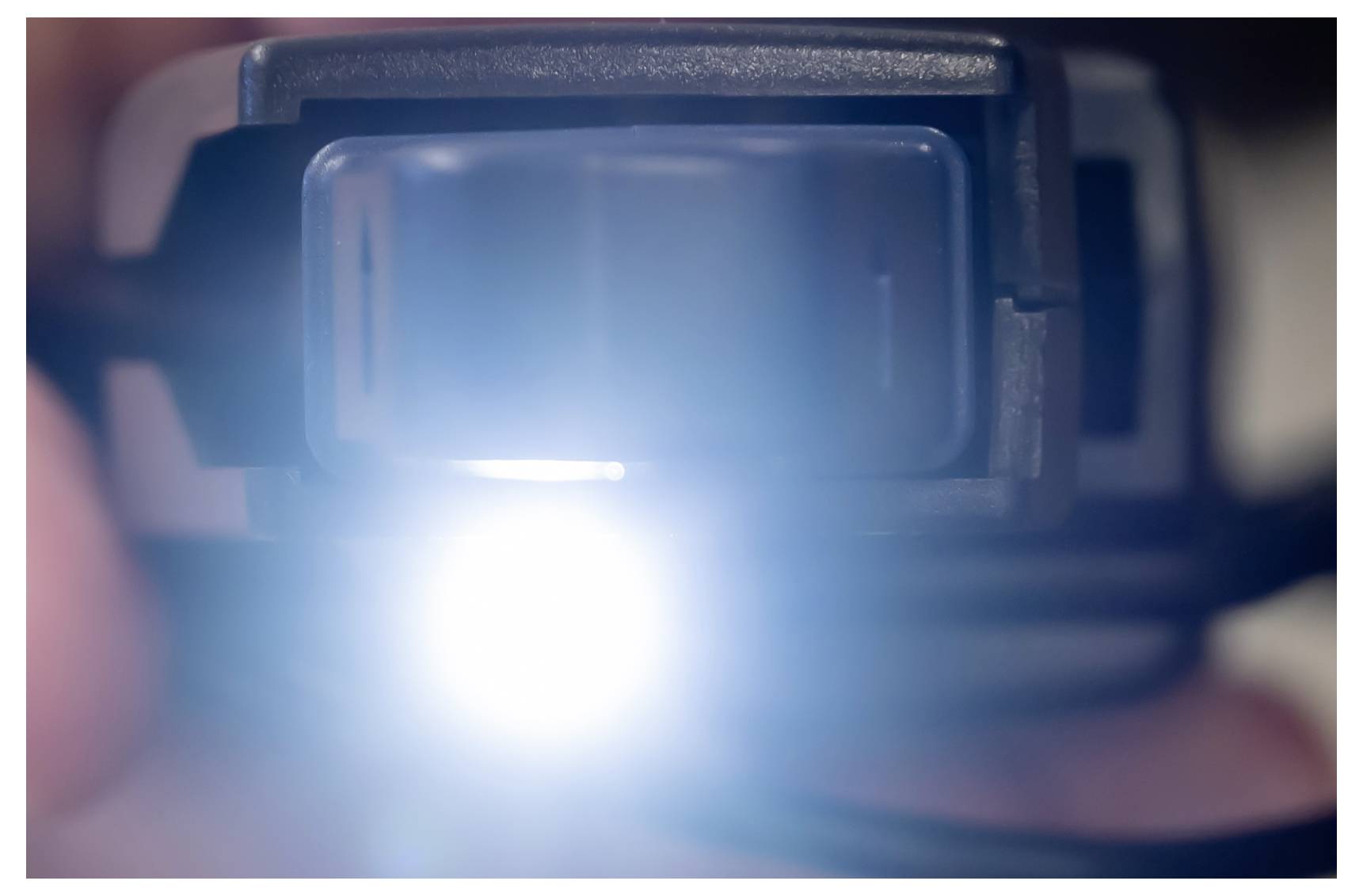 Close-up of a camera or device lens emitting a bright white light, with the surrounding housing blurred in soft focus.