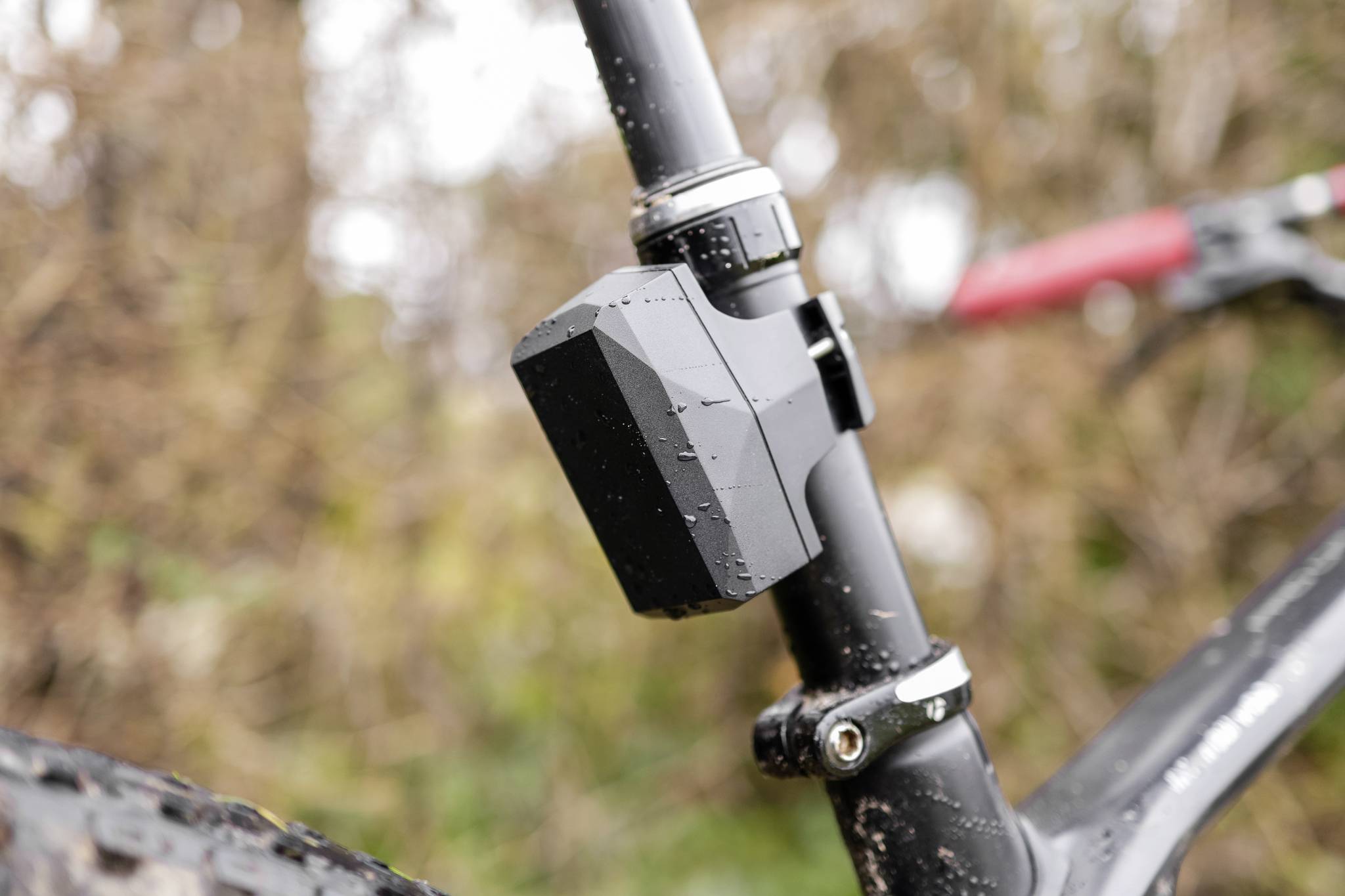 Close-up of a black and grey bicycle component on a metal frame. Dirt and water droplets are visible. Background is out of focus.