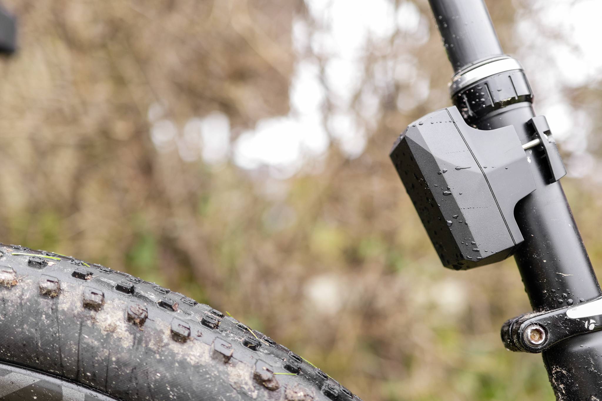 Close-up of a bicycle with a mud-splattered tyre. Focus on the suspension fork, which is wet from the rain.