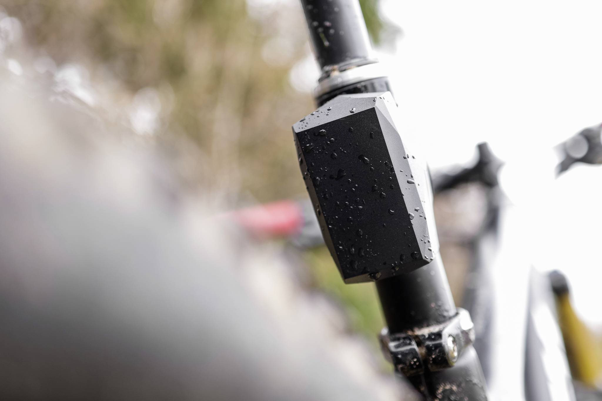 Close-up of a black bicycle fork with water droplets. Backgrounds are blurred, suggesting rainy weather.