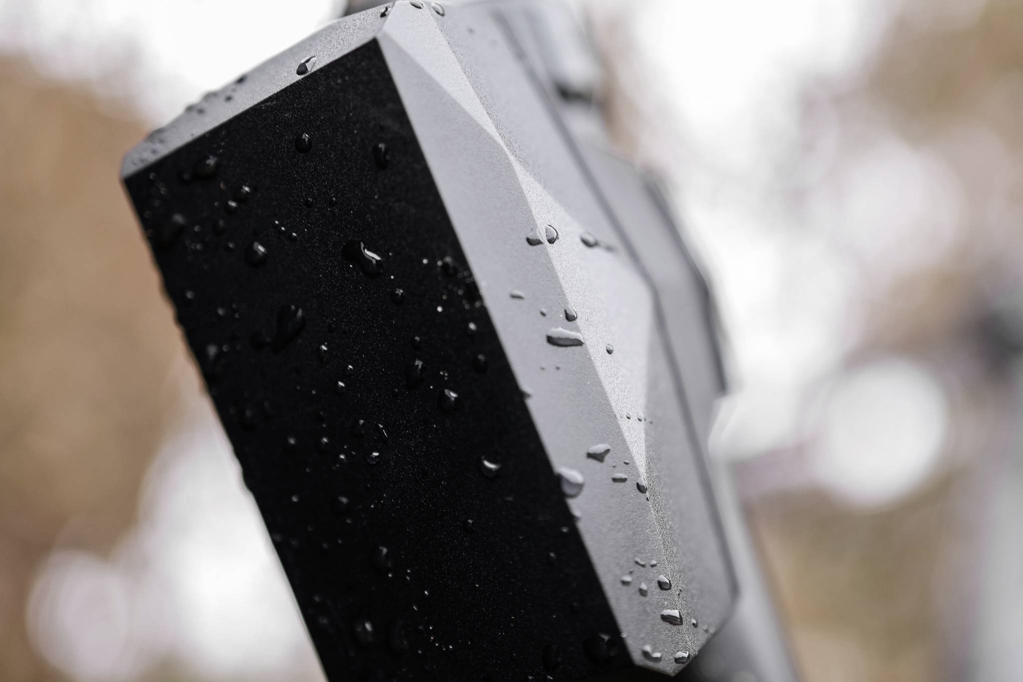 Close-up of a black, rain-covered rectangle with geometric shapes, blurred background with warm colour tones.