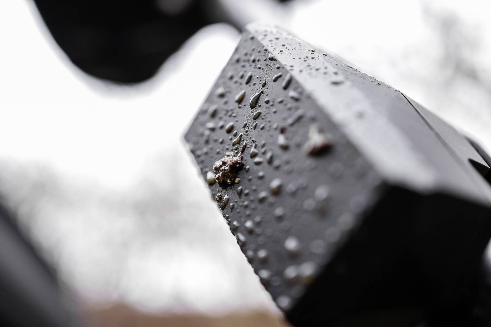 Close-up of a rain-soaked surface texture of an exterior object, possibly a casing or device, with water droplets.