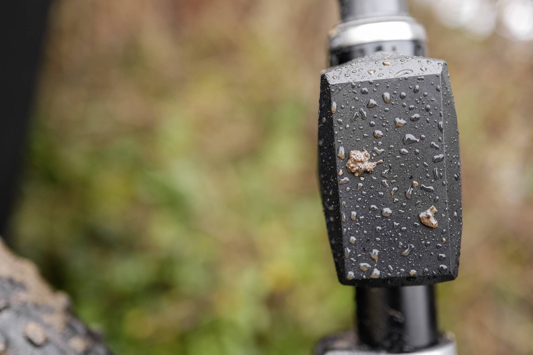 Close-up of a bicycle handlebar with raindrops on it, blurred green in the background.