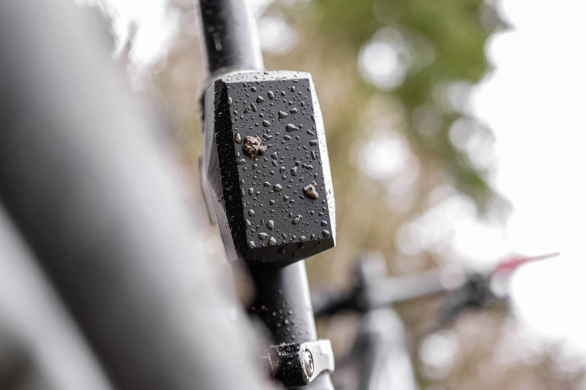 Close-up of a black-painted bicycle frame with water droplets, blurred natural background.