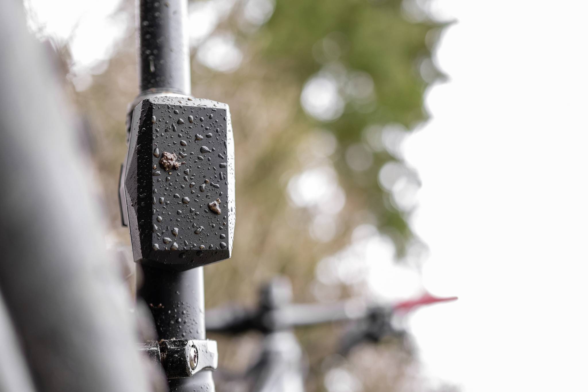 Close-up of a bicycle with raindrops on the metal frame, with a blurred green landscape in the background.
