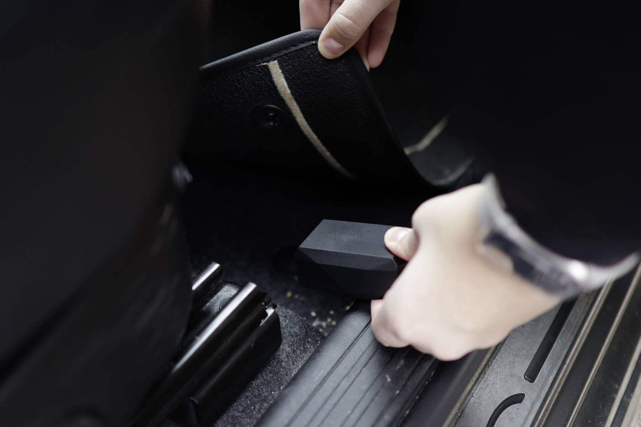 A person lifts a car floor mat and discovers a hidden object underneath.